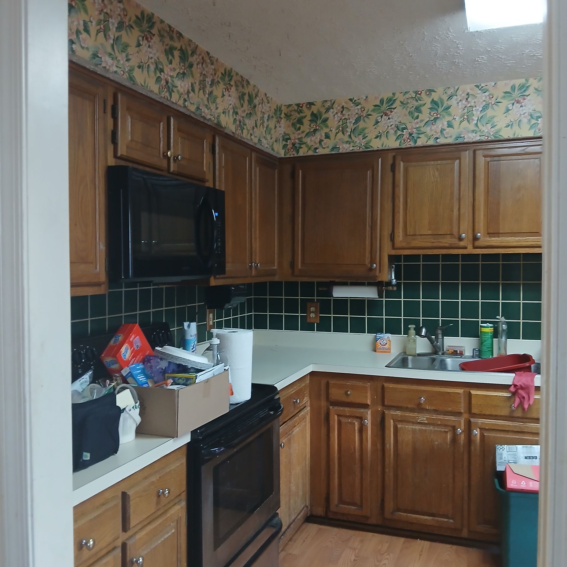 Cluttered kitchen with wooden cabinets, black appliances, and green tile backsplash