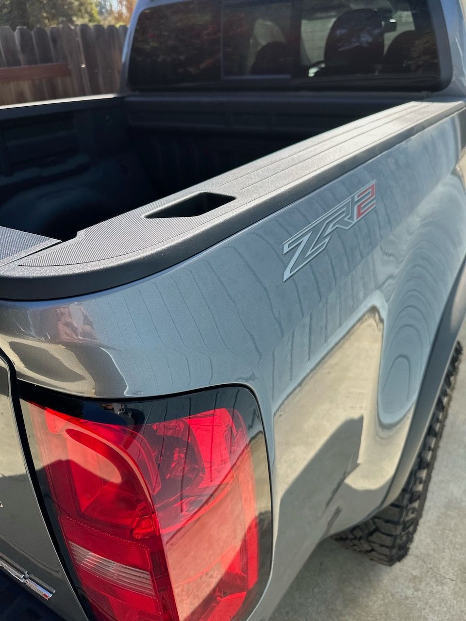 Gray Chevrolet ZR2 truck bed, taillight, and rear fender, viewed from a high angle outdoors.
