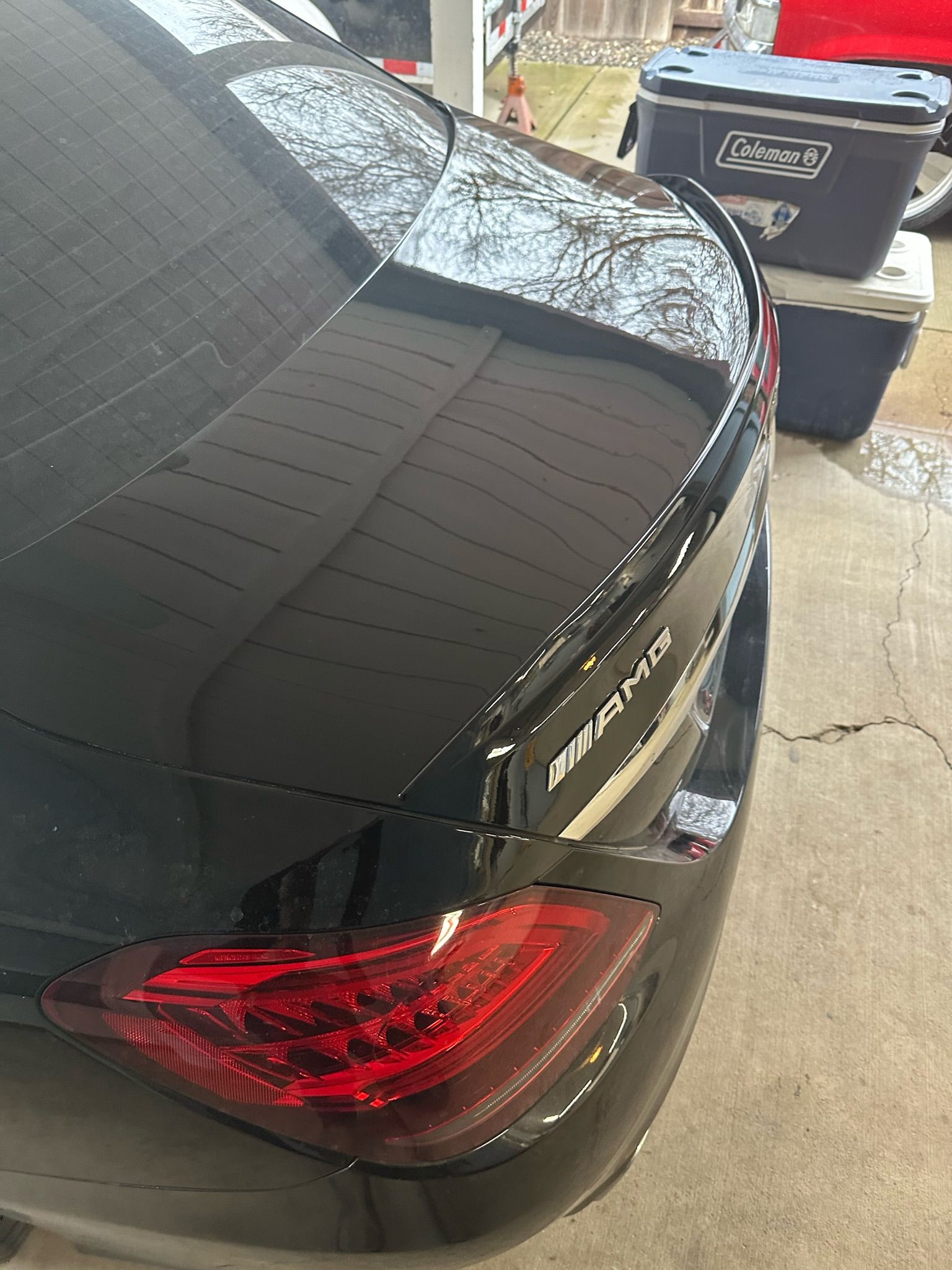 A close-up, high-angle shot of the rear of a black Mercedes-Benz AMG sedan, featuring a lip spoiler and taillight.