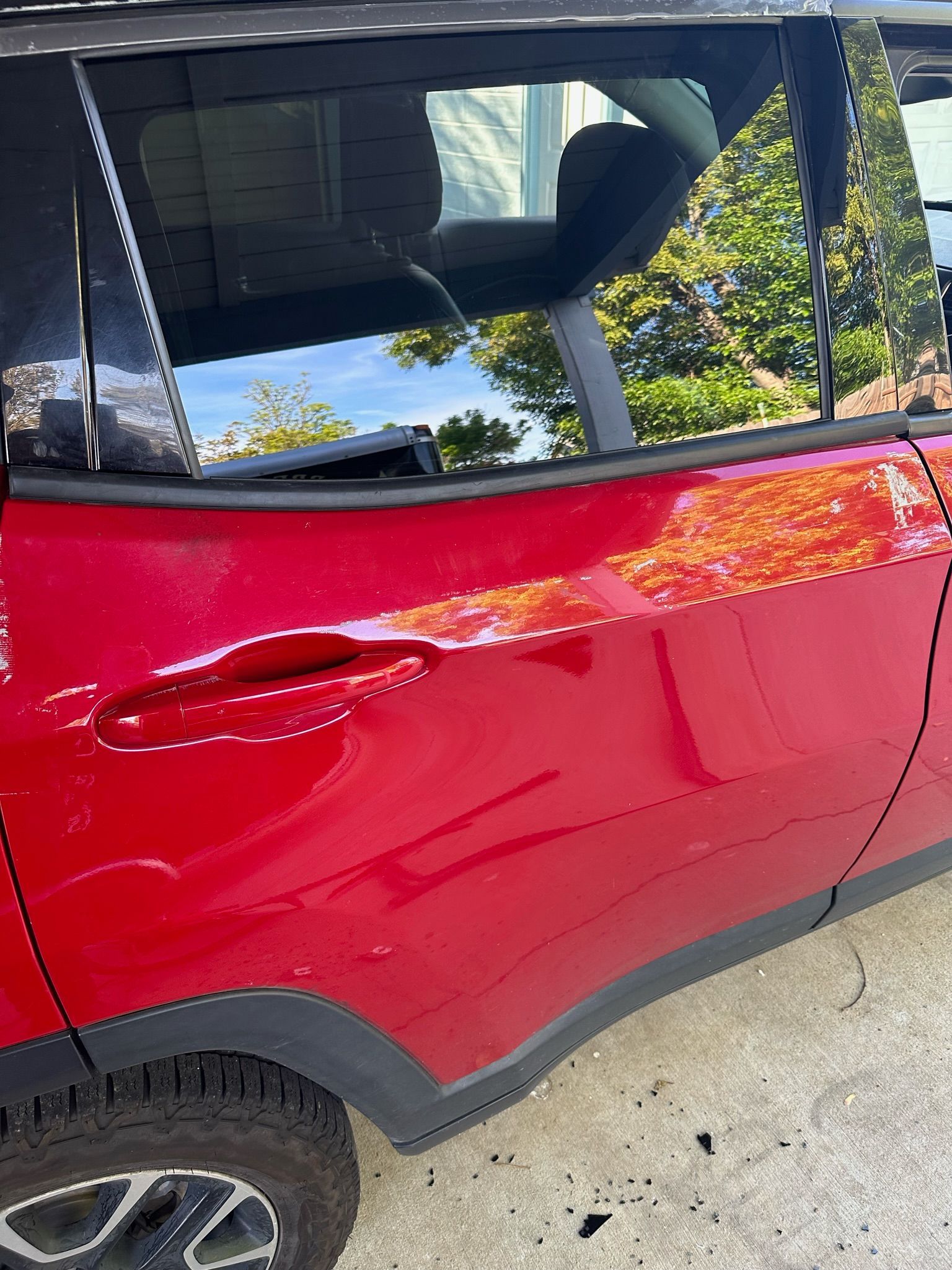 A red car with a damaged door is parked on the side of the road.