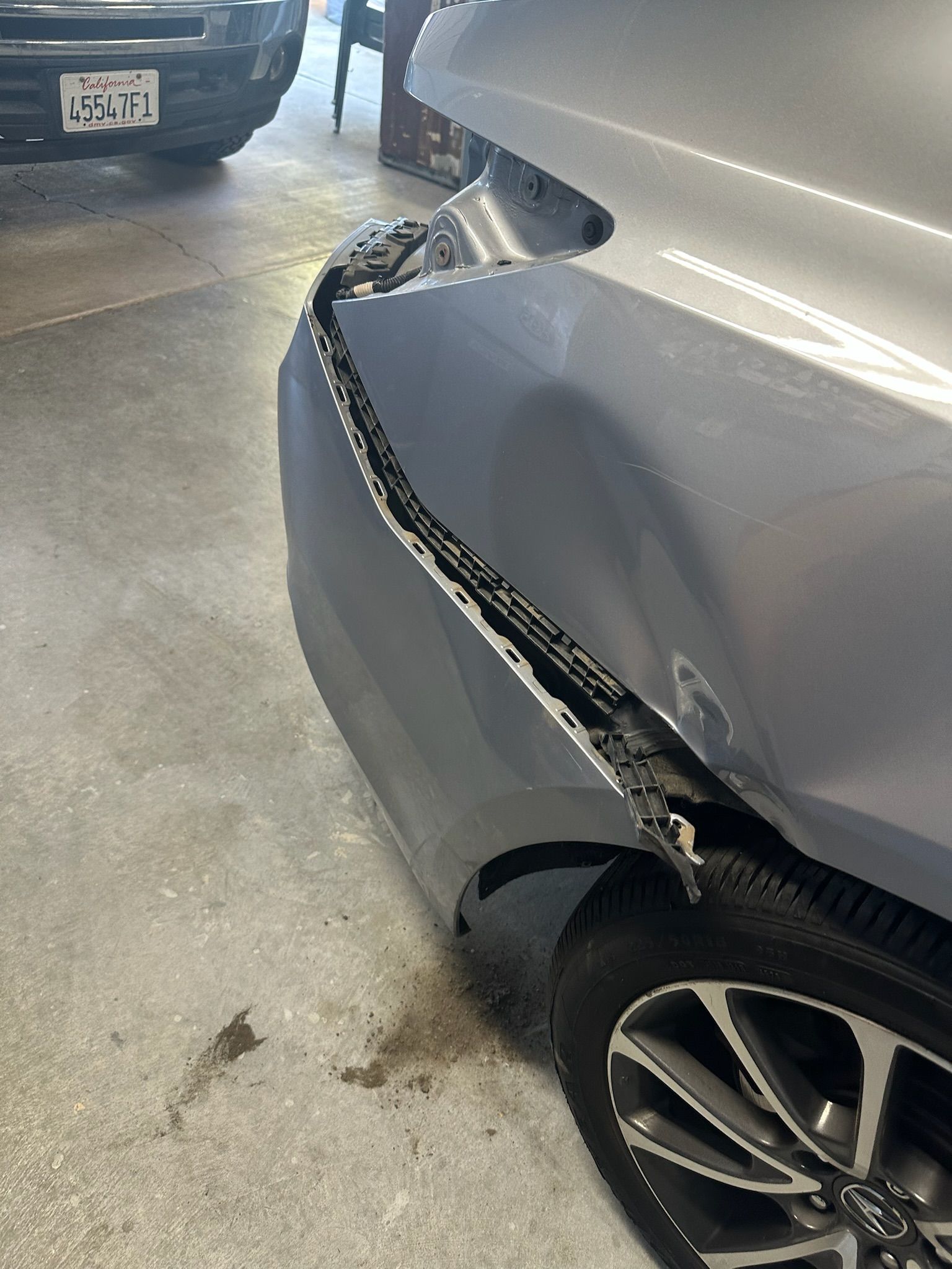 A car with a damaged bumper is parked in a garage.