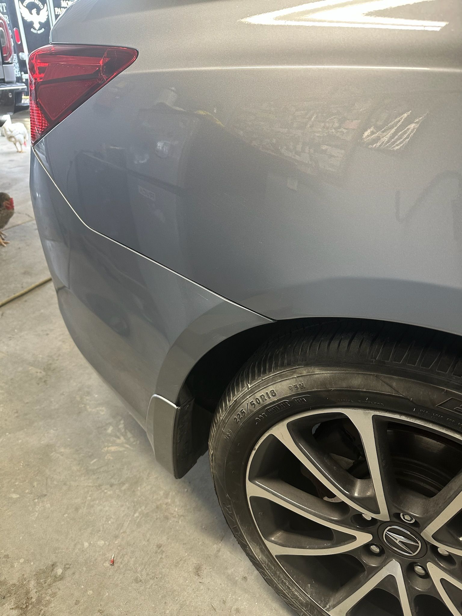 A close-up view of the rear quarter panel of a gray car, showing light scratches or scuffs along the wheel arch.