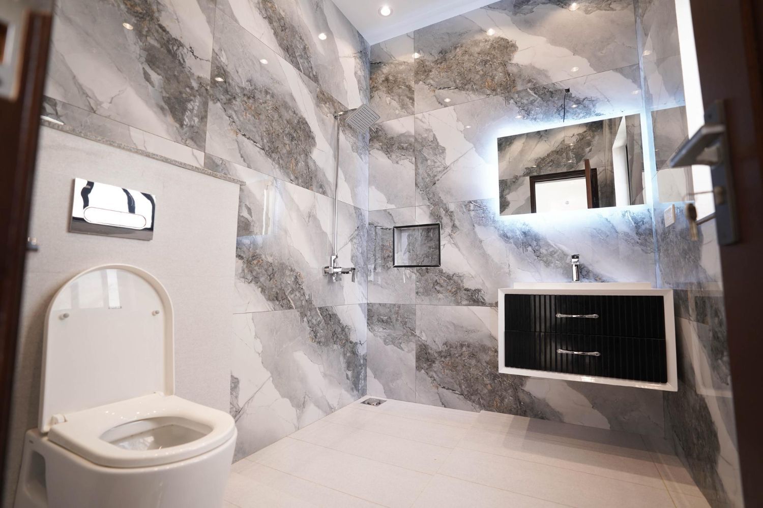 Modern bathroom with gray marble walls, wall-mounted sink, mirror, and toilet