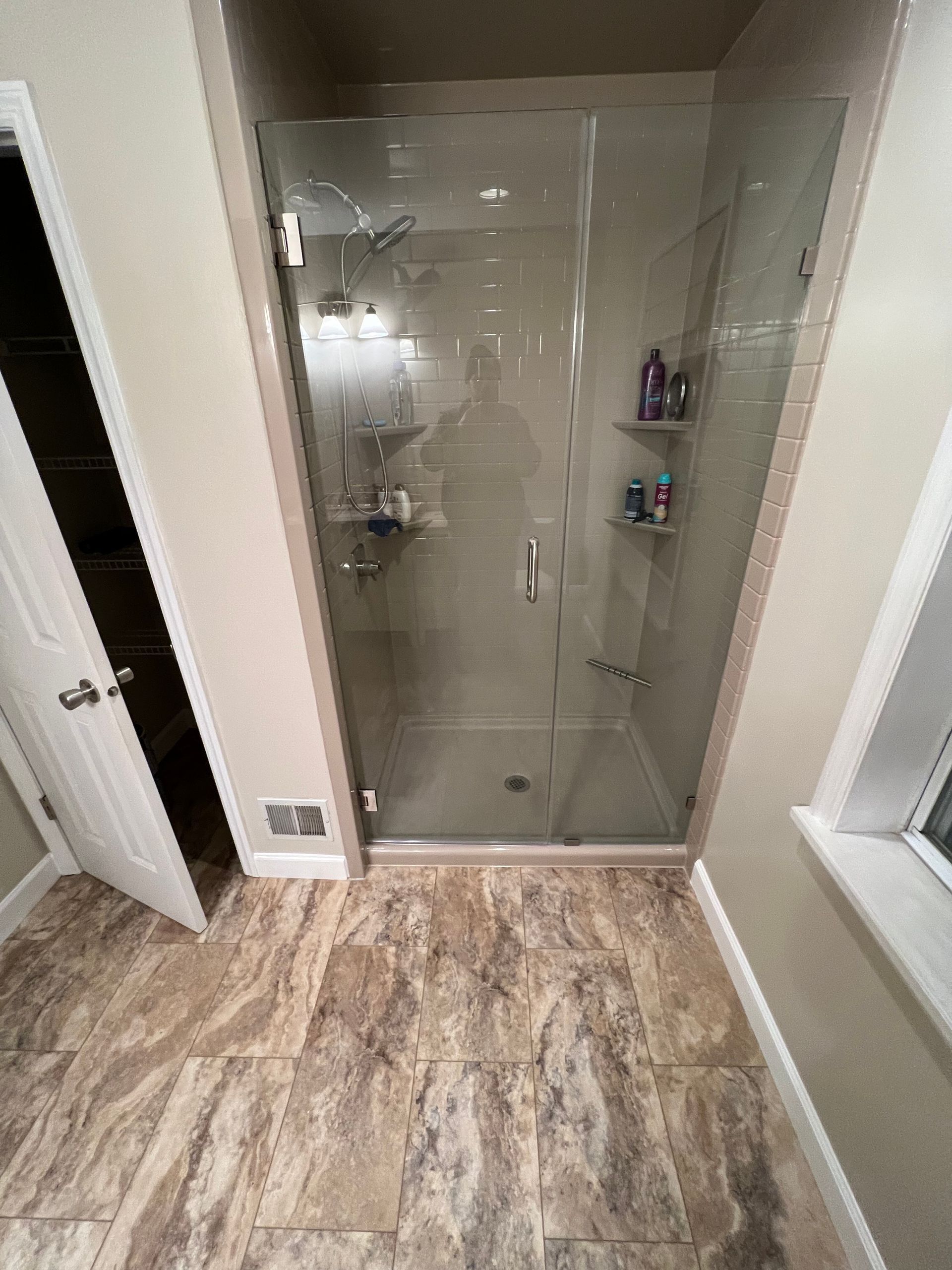 Bathroom with a glass shower enclosure, marble-look tile floor, and beige walls.