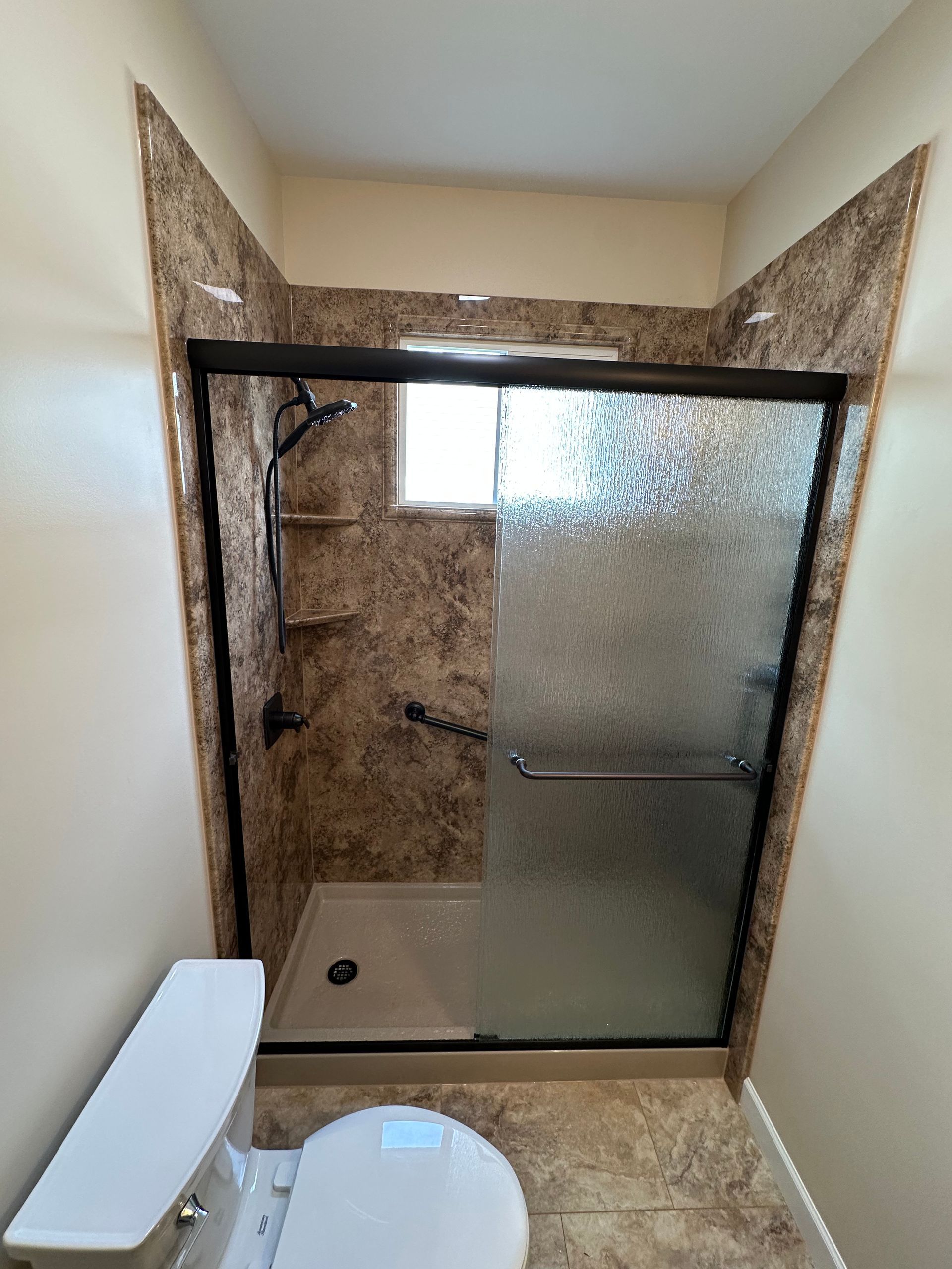 Bathroom with tiled walk-in shower, frosted glass door, black fixtures, and toilet.