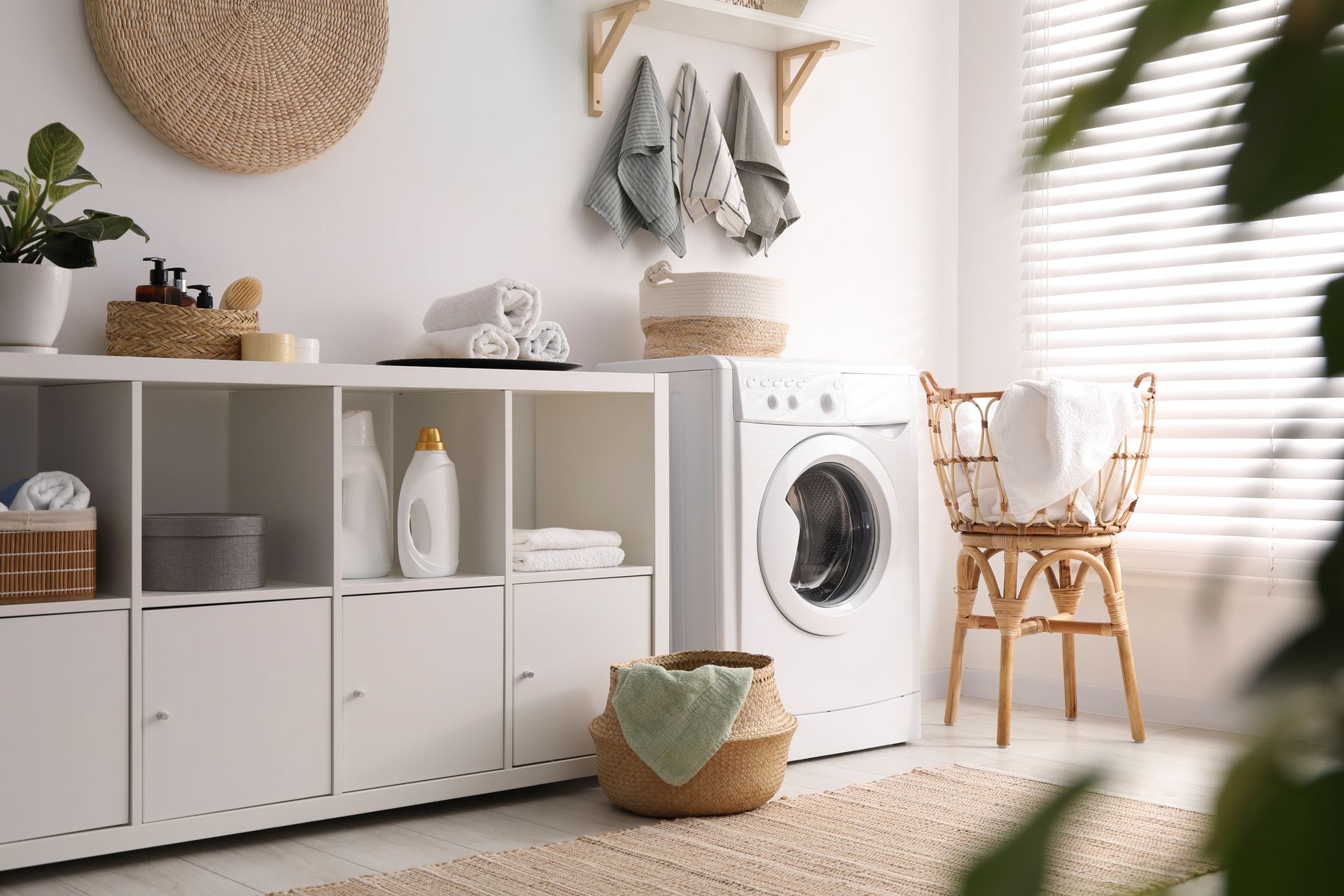 Bright organized laundry room with washer, folded towels, baskets, and hanging linens.