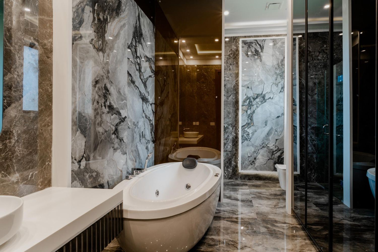 Modern marble bathroom with freestanding oval tub, glass shower, and warm lighting