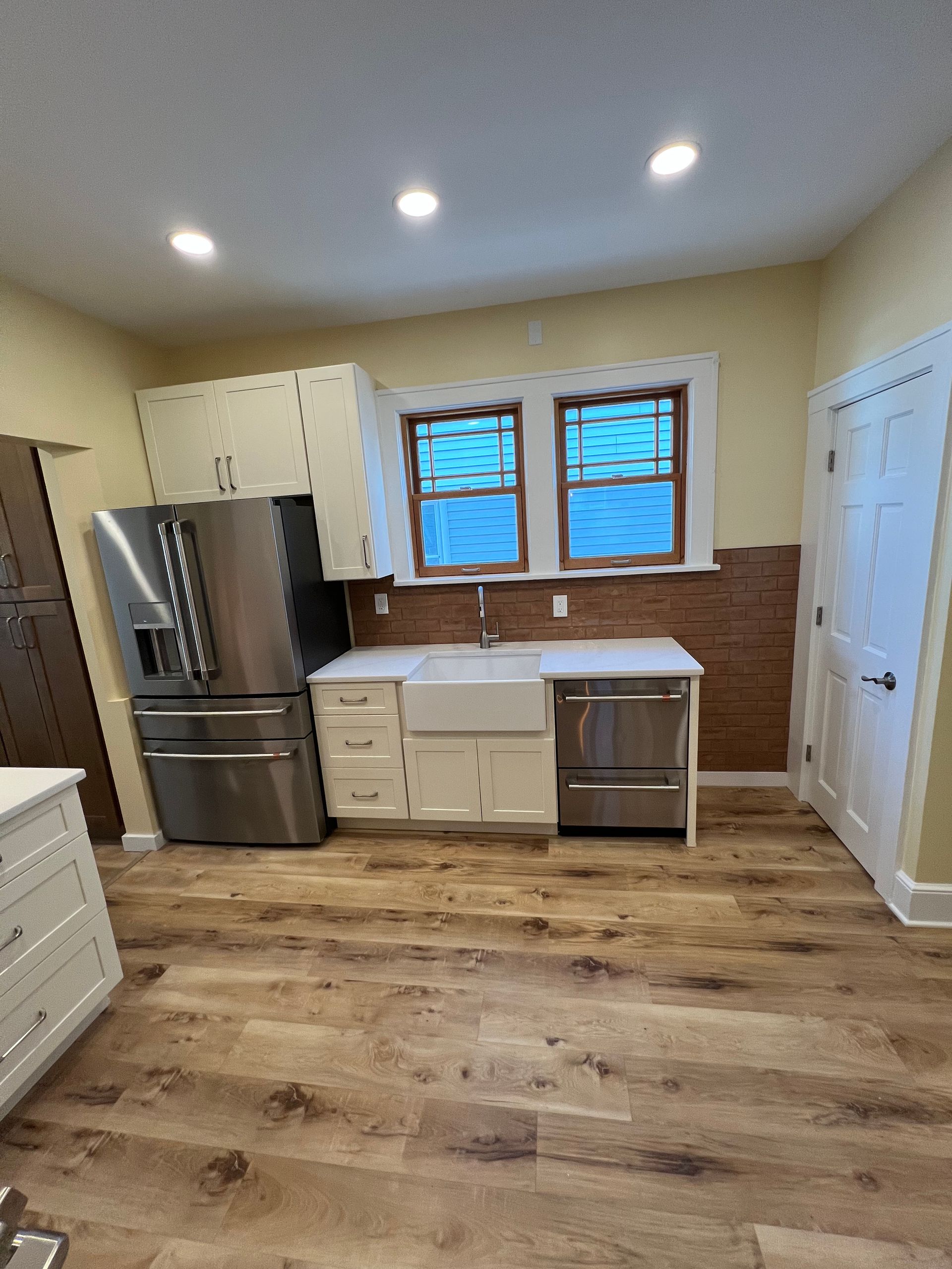 Modern kitchen with white cabinets, stainless appliances, farmhouse sink, and wood floors.