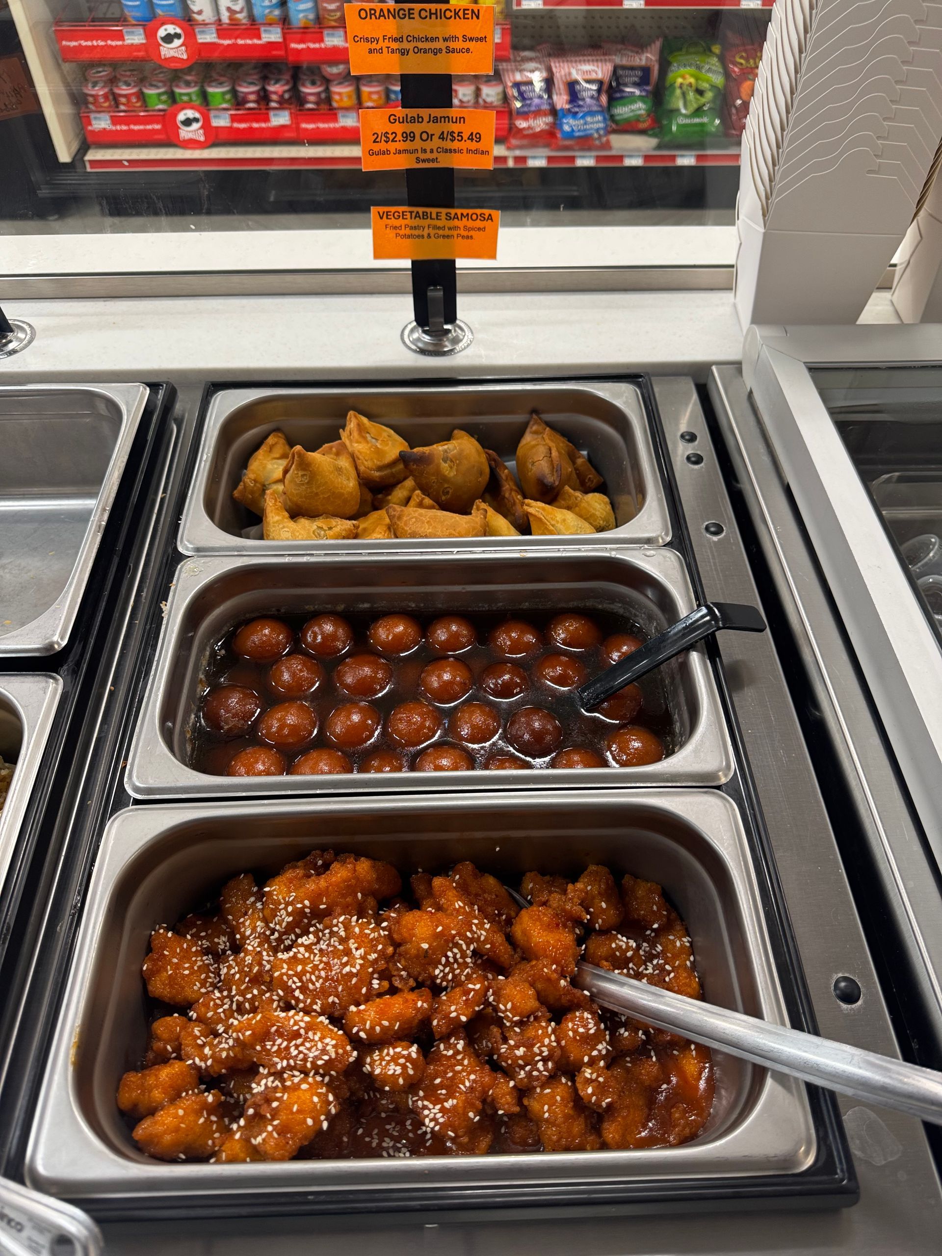 Food display with three metal containers: fried pastries, dark spheres, and orange chicken.