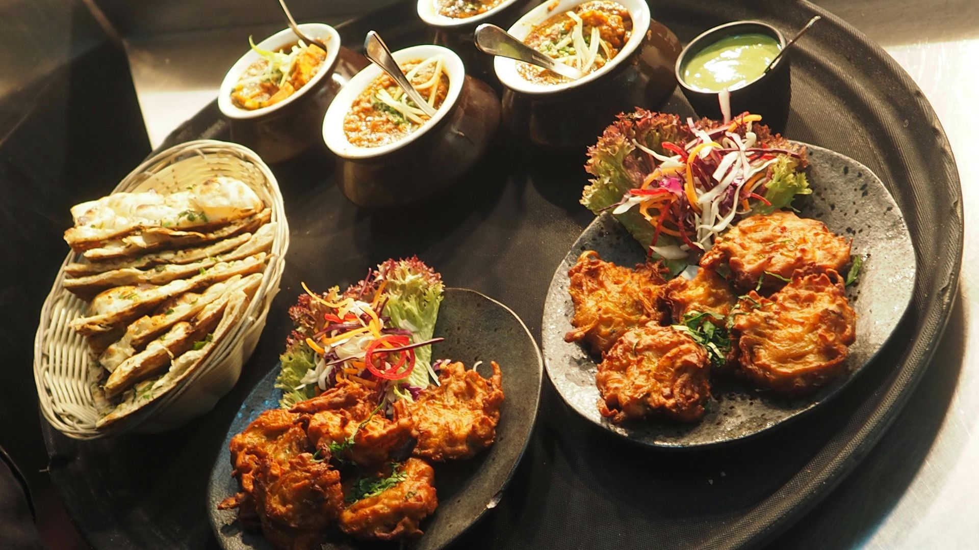 Tray of Indian dishes including curries, pakoras, naan bread, and a green sauce.