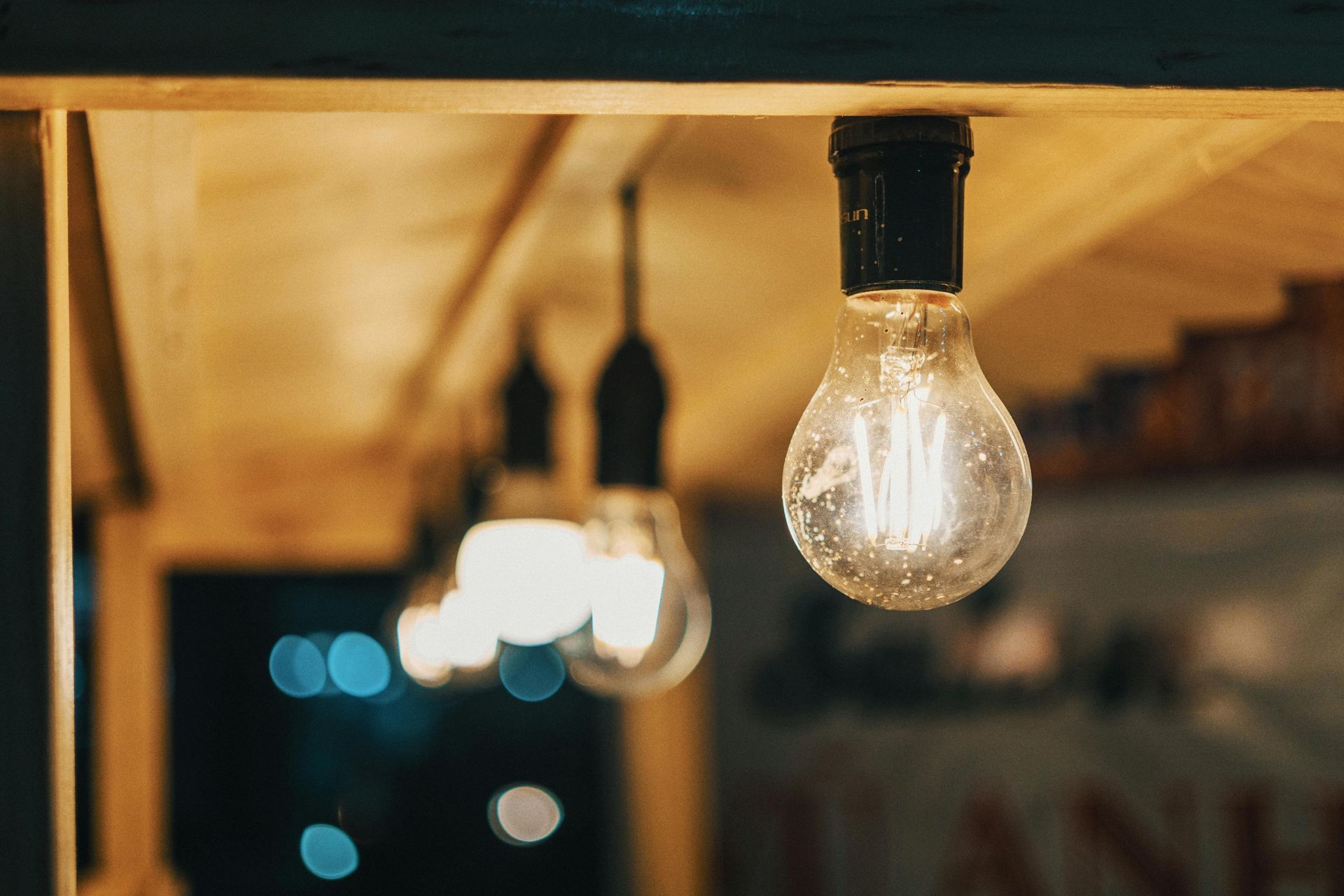 Row of lit, teardrop-shaped light bulbs hanging from a wooden structure, against blurred night background.