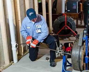 A man in a blue shirt is working on a drain in a basement.