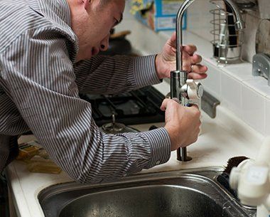 Man repairing a kitchen faucet over a sink with tools and running water nearby