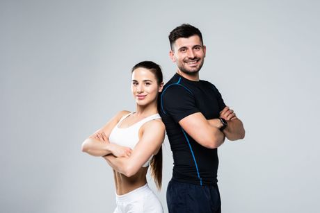 A man and a woman are standing back to back with their arms crossed.