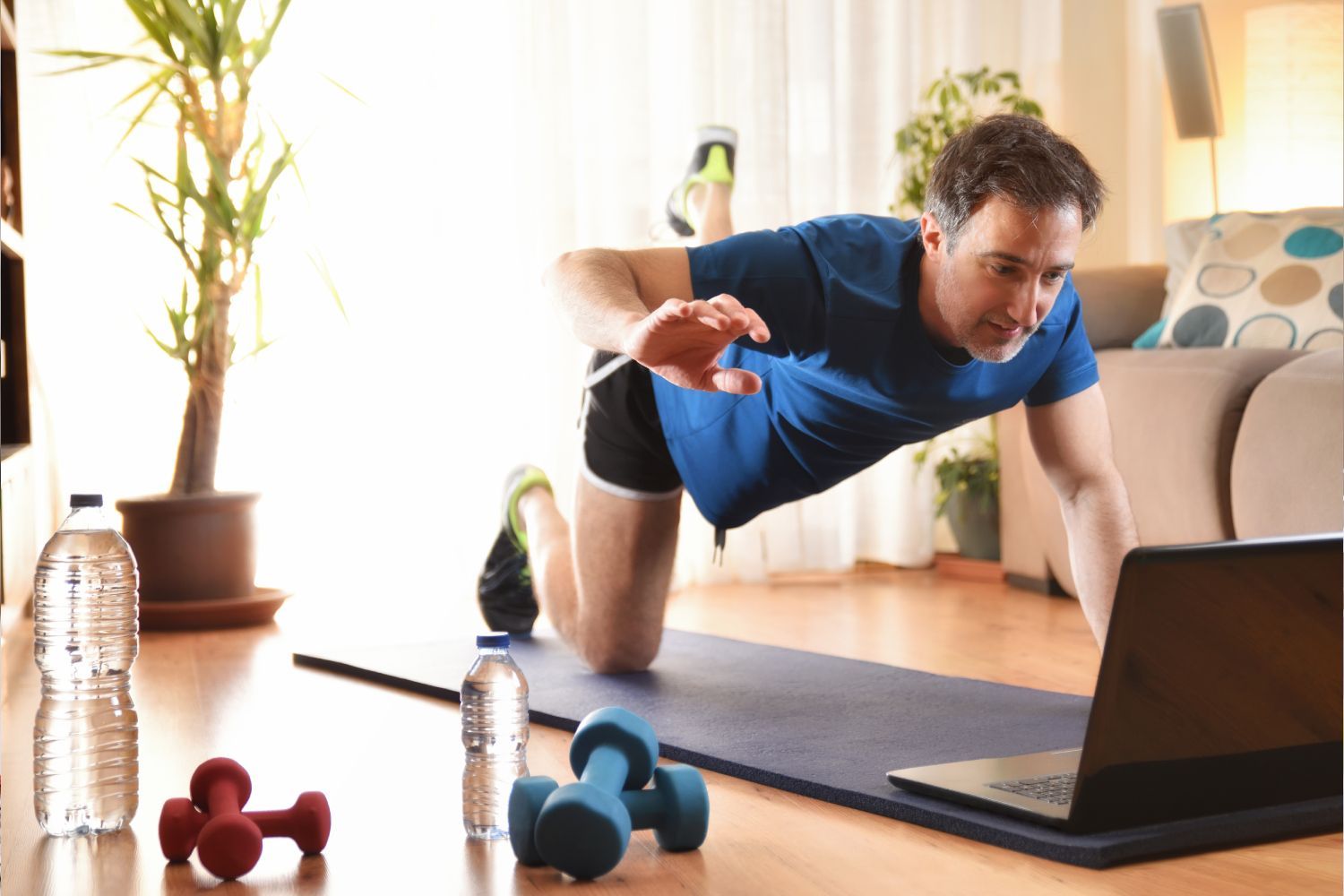 A man is doing push ups on a yoga mat in front of a laptop computer.