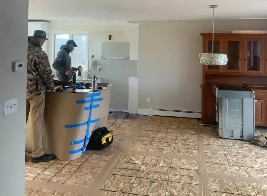 Two men are working on a kitchen island with blue tape.