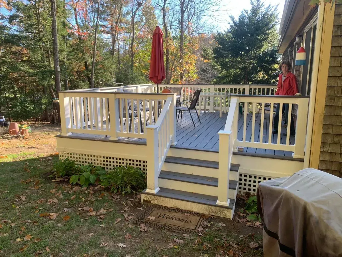 A man in a red jacket is standing on a deck next to a grill.