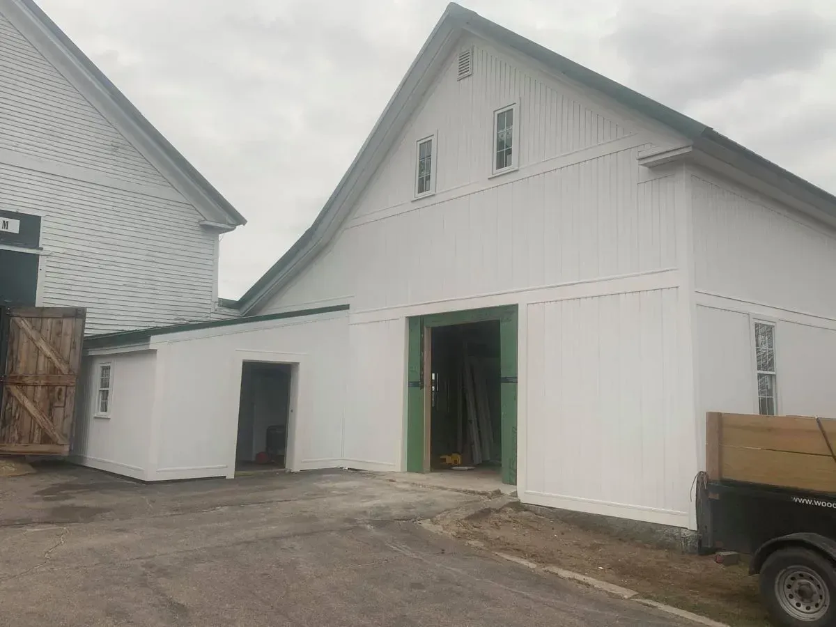 A white barn with a green door and a truck parked in front of it.