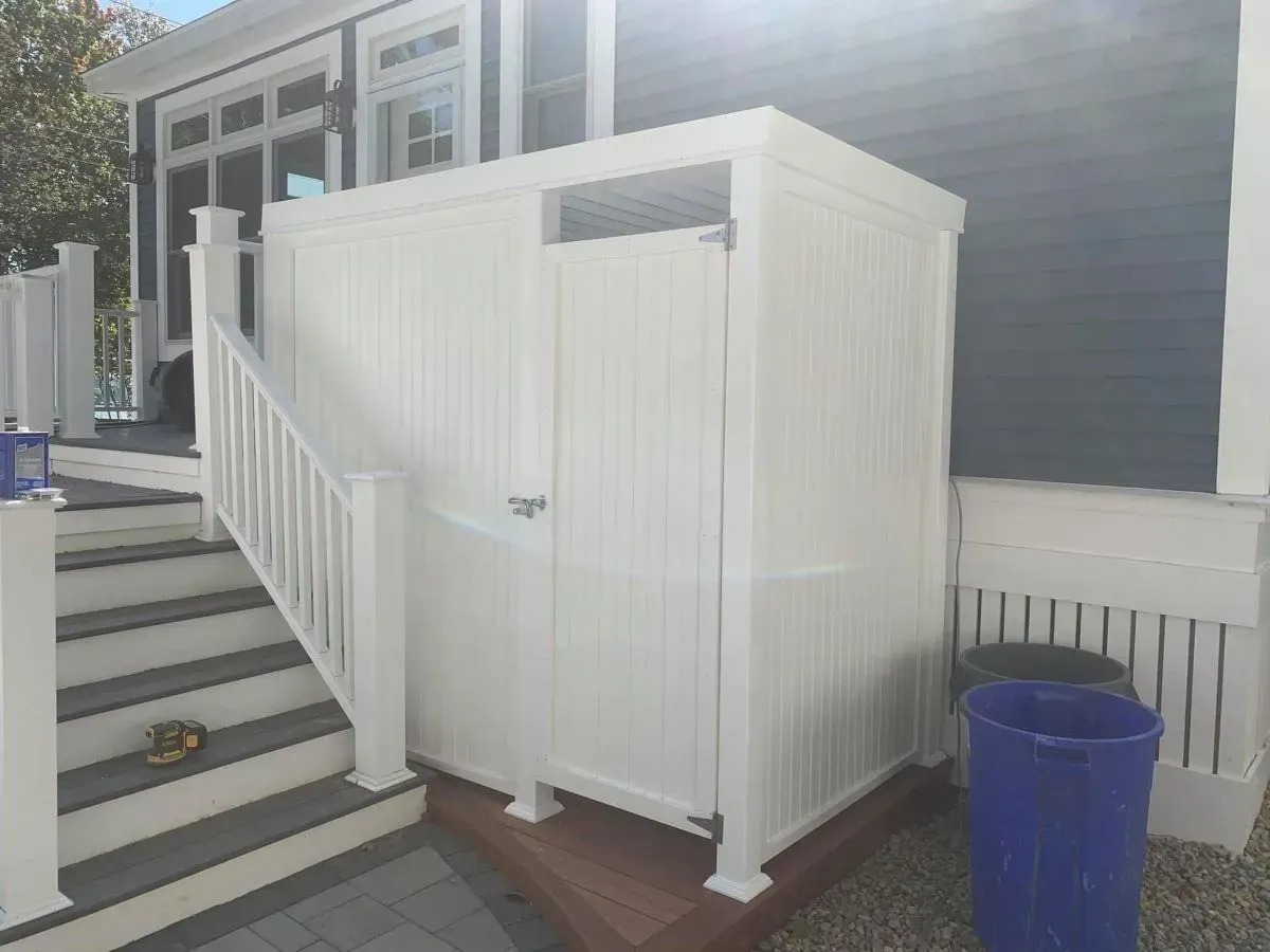 A white fence is sitting on the side of a house next to stairs.