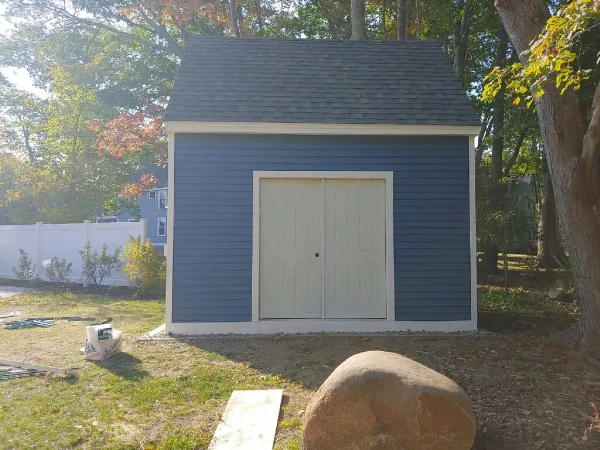 A blue and white shed is sitting in the middle of a grassy yard.