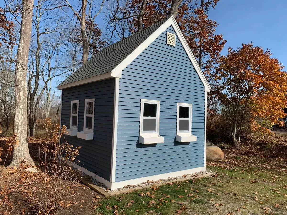 A blue and white shed with two windows is sitting in the middle of a field.