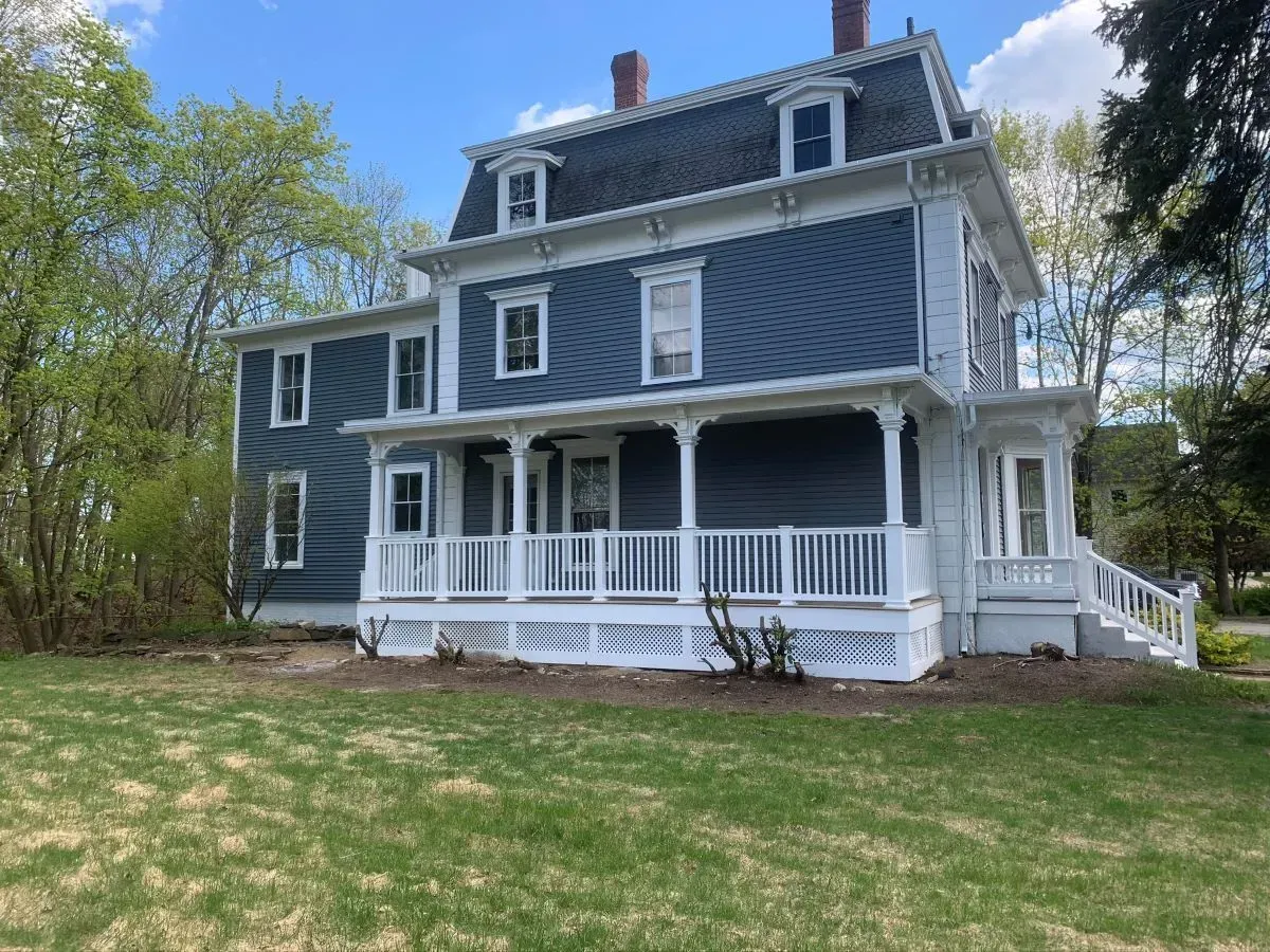 A large house with a large porch is sitting on top of a lush green field.