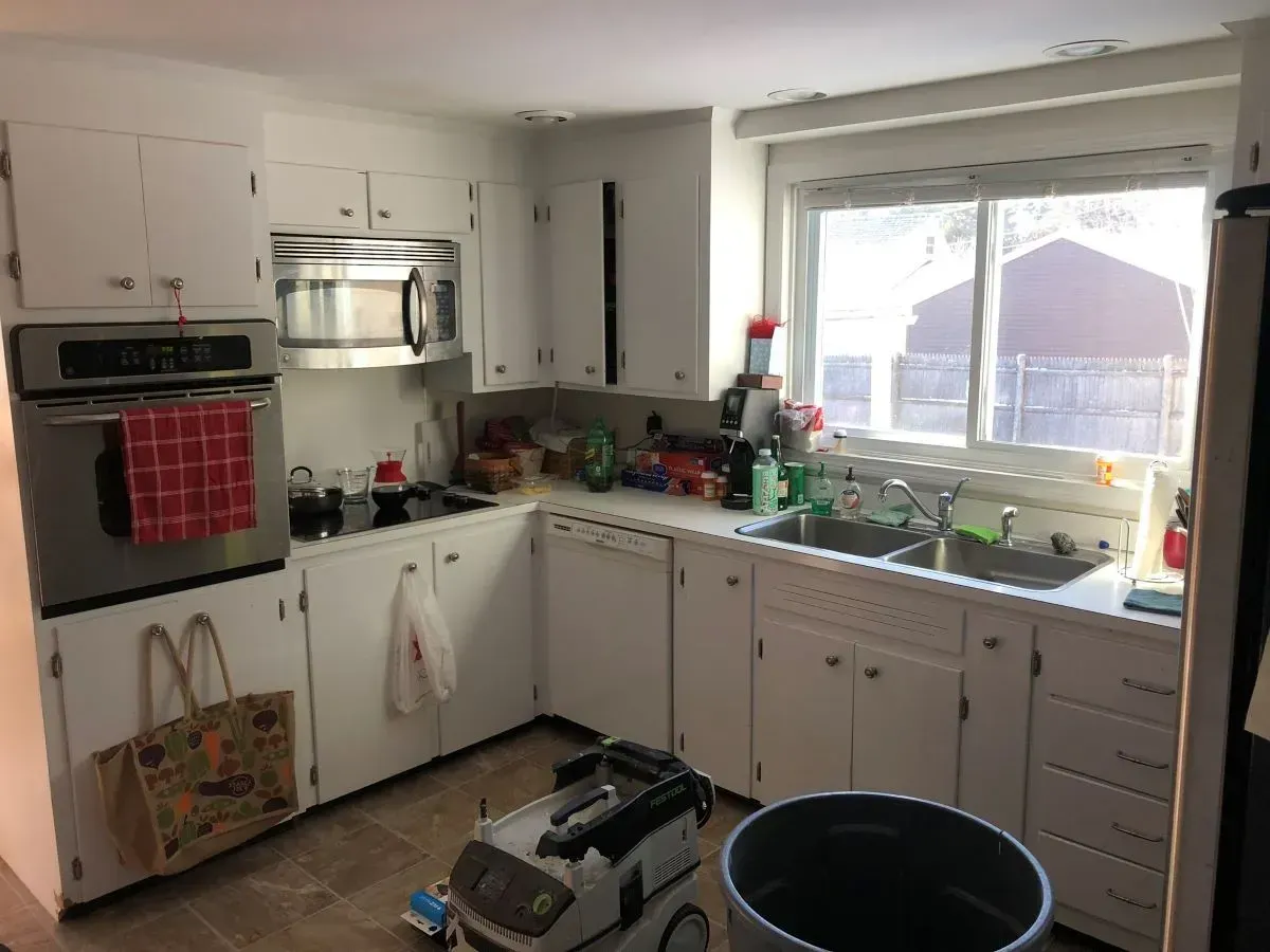A kitchen with white cabinets , a microwave , a sink , and a window.