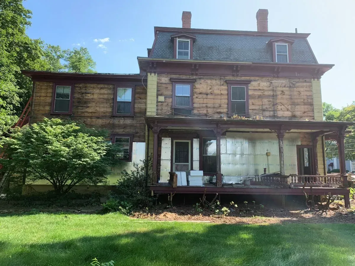 A large house with a porch and a lot of windows is sitting on top of a lush green field.