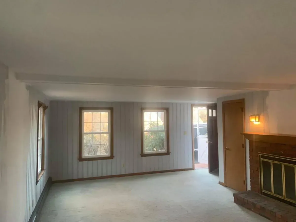 An empty living room with a fireplace and three windows.