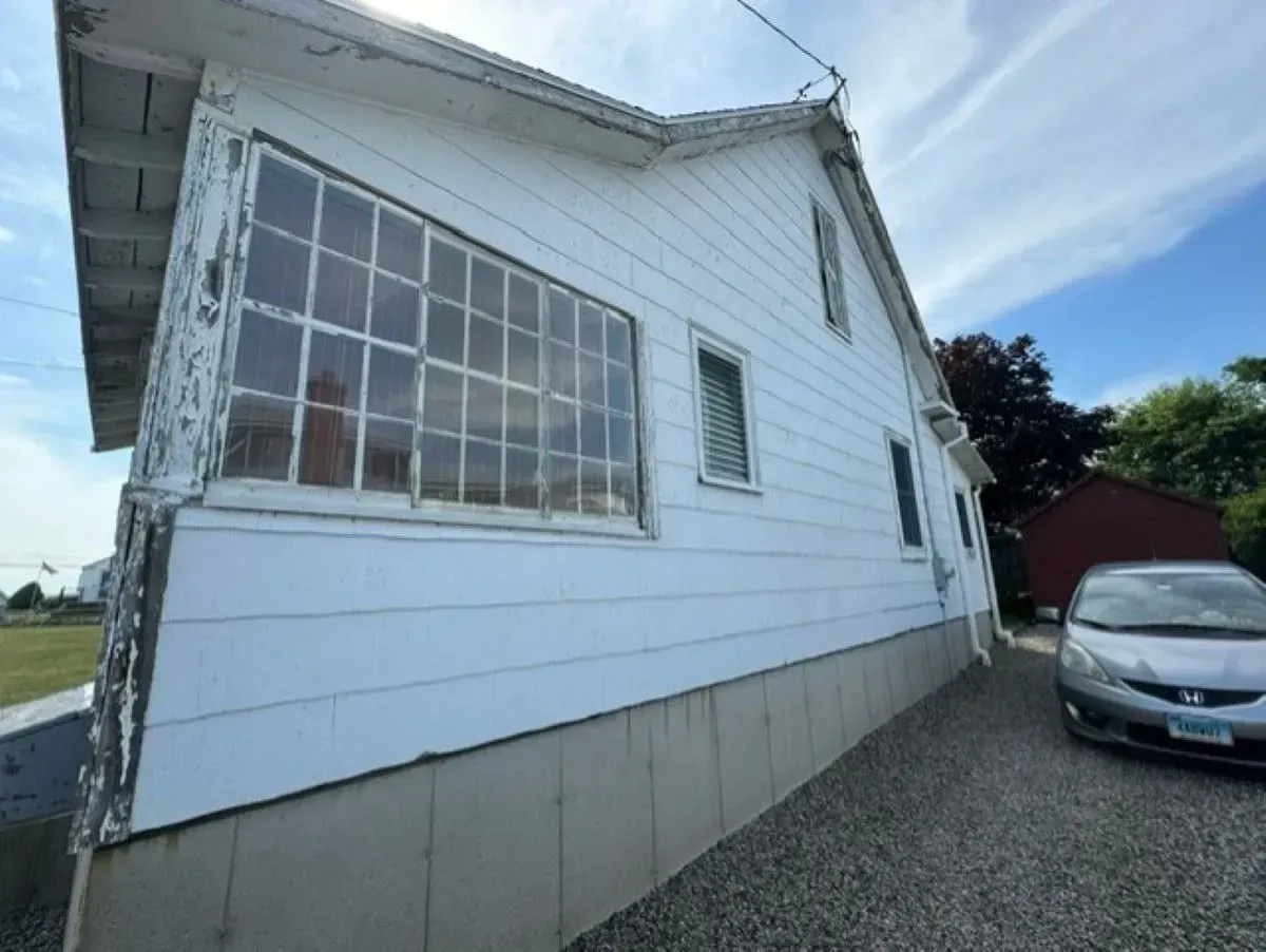 A man is standing next to a wheelbarrow in front of a house