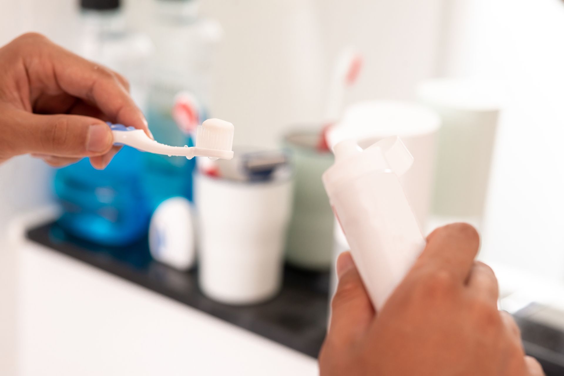 Hands brushing teeth with toothpaste in a bathroom sink area