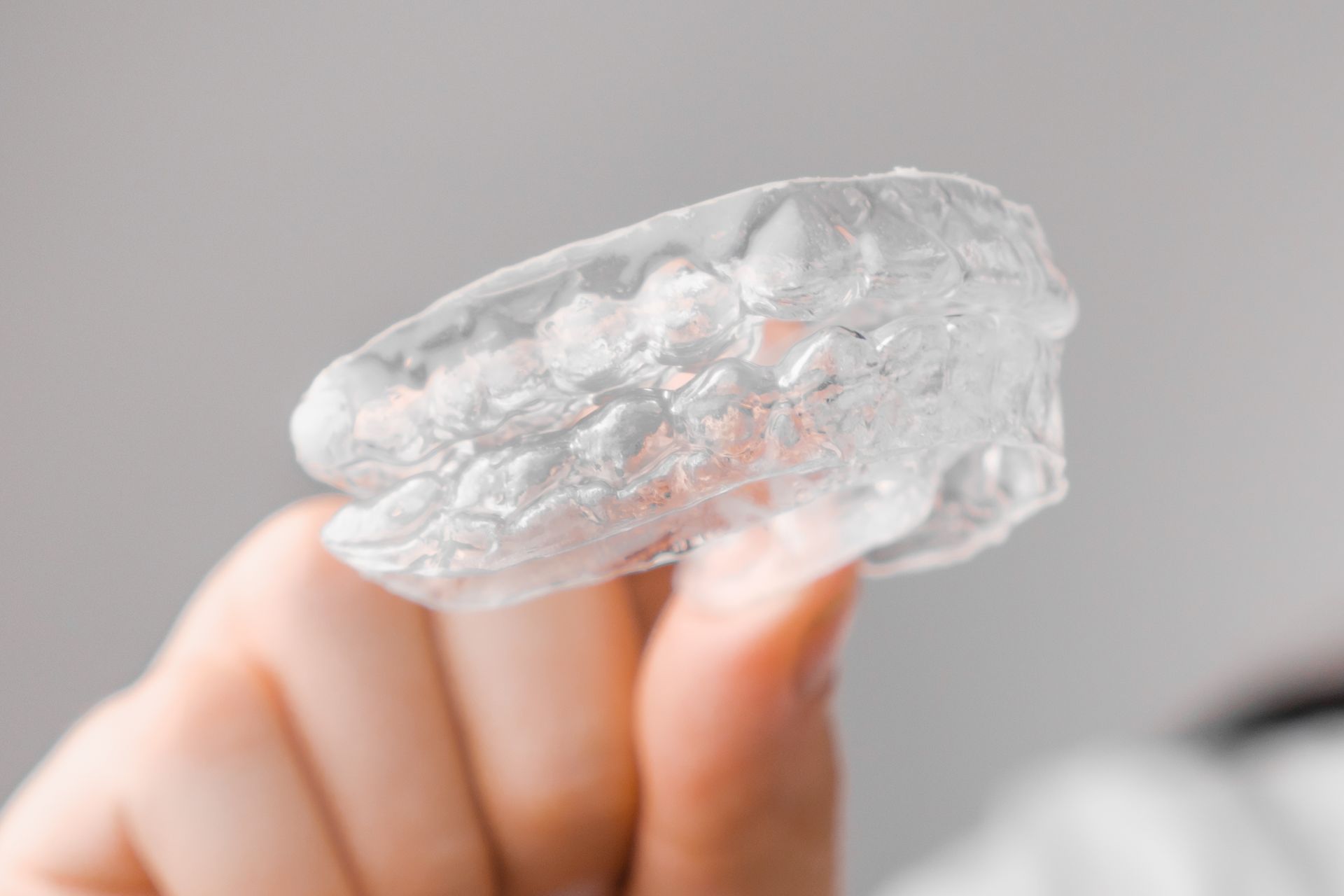 A hand holding a clear, irregular ice cube against a soft gray background
