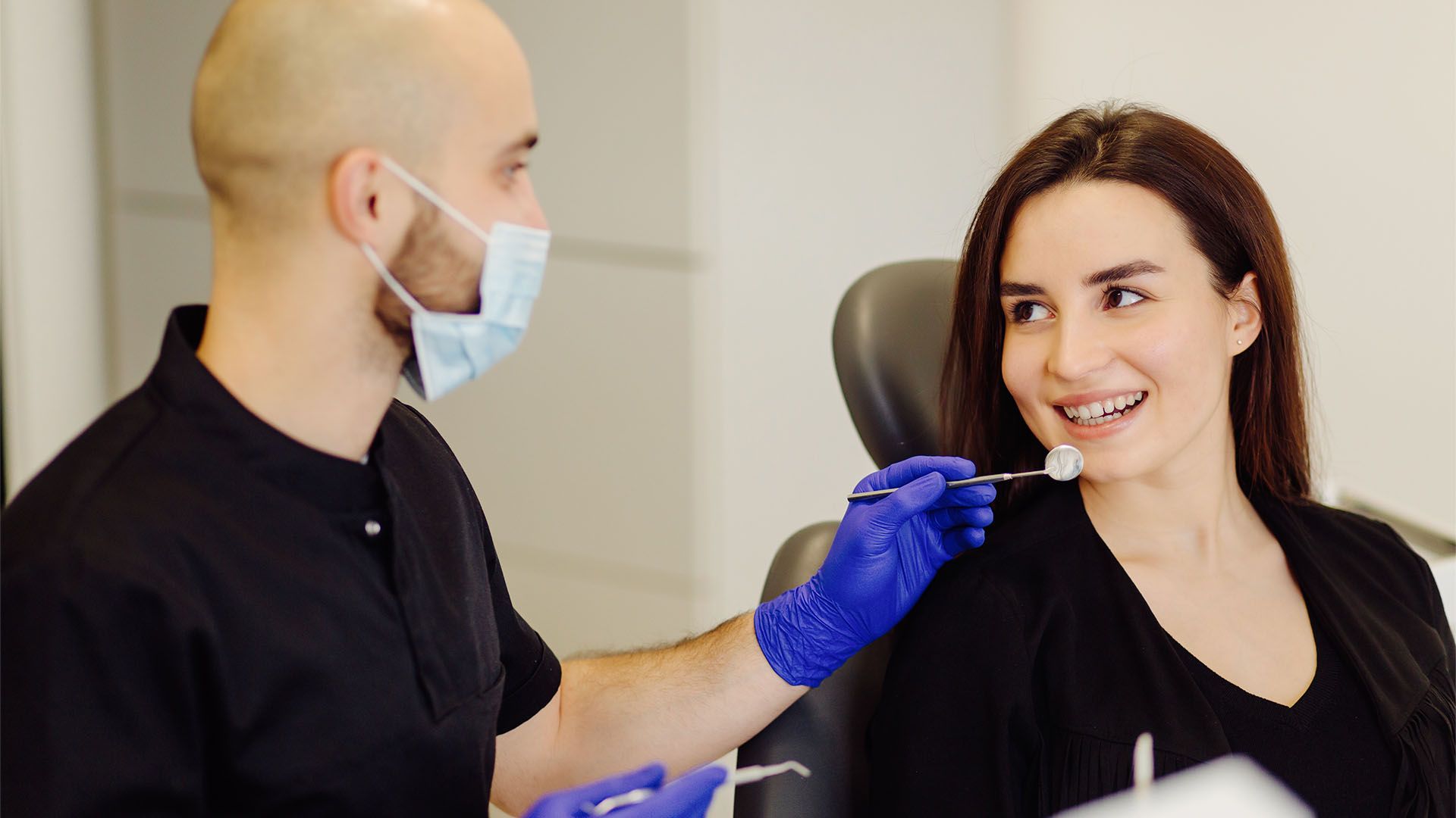 Dentist examining a patient's teeth with a mirror. They are in an office setting.