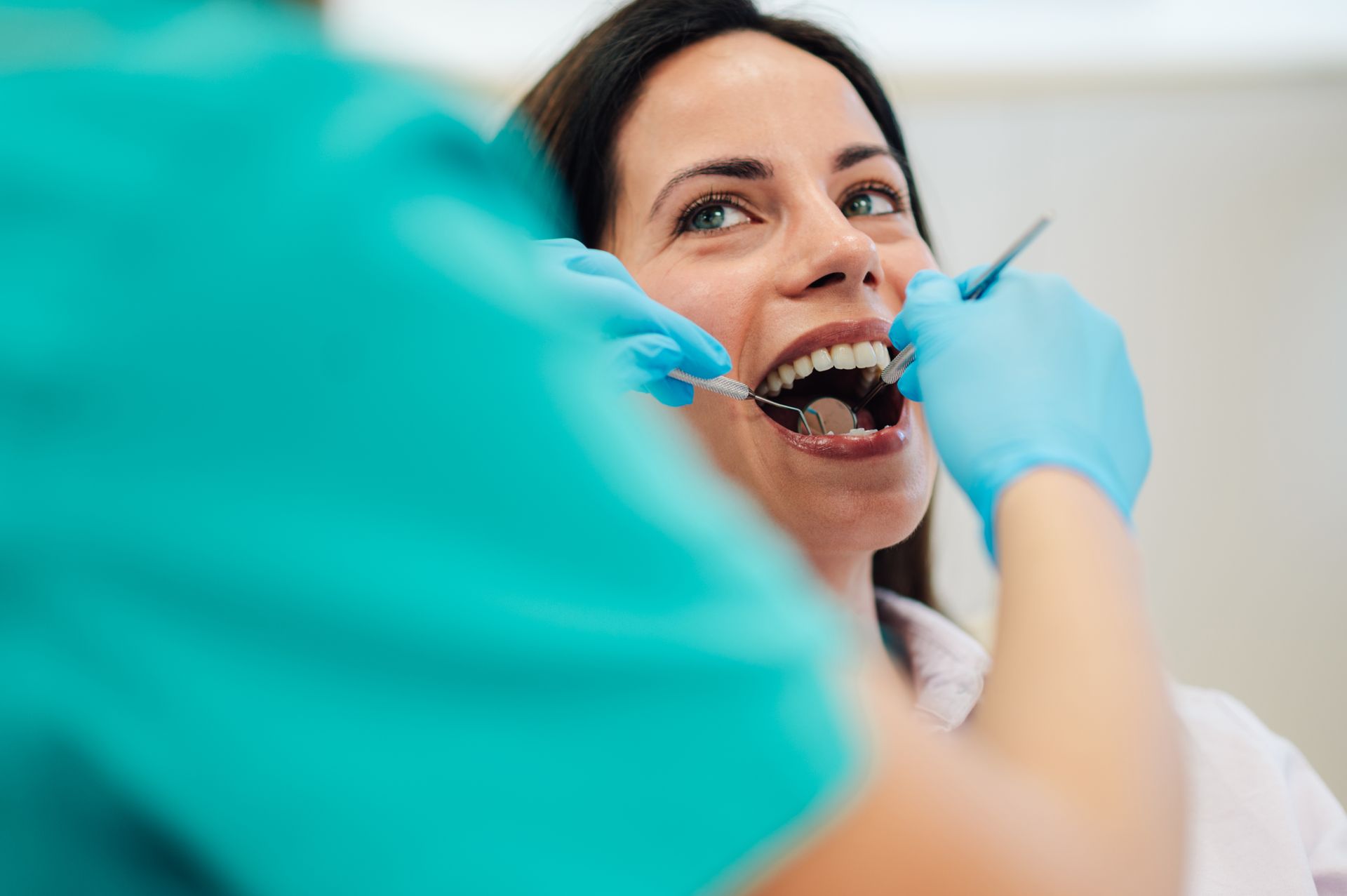 Dentist examining a smiling patient’s teeth with blue gloves and dental tools