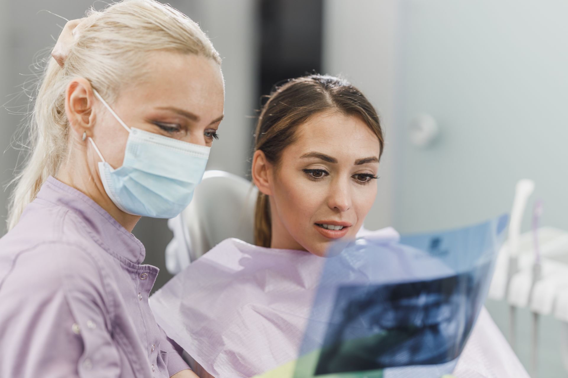 Two women reviewing an X-ray in a medical clinic, one wearing a mask and gloves