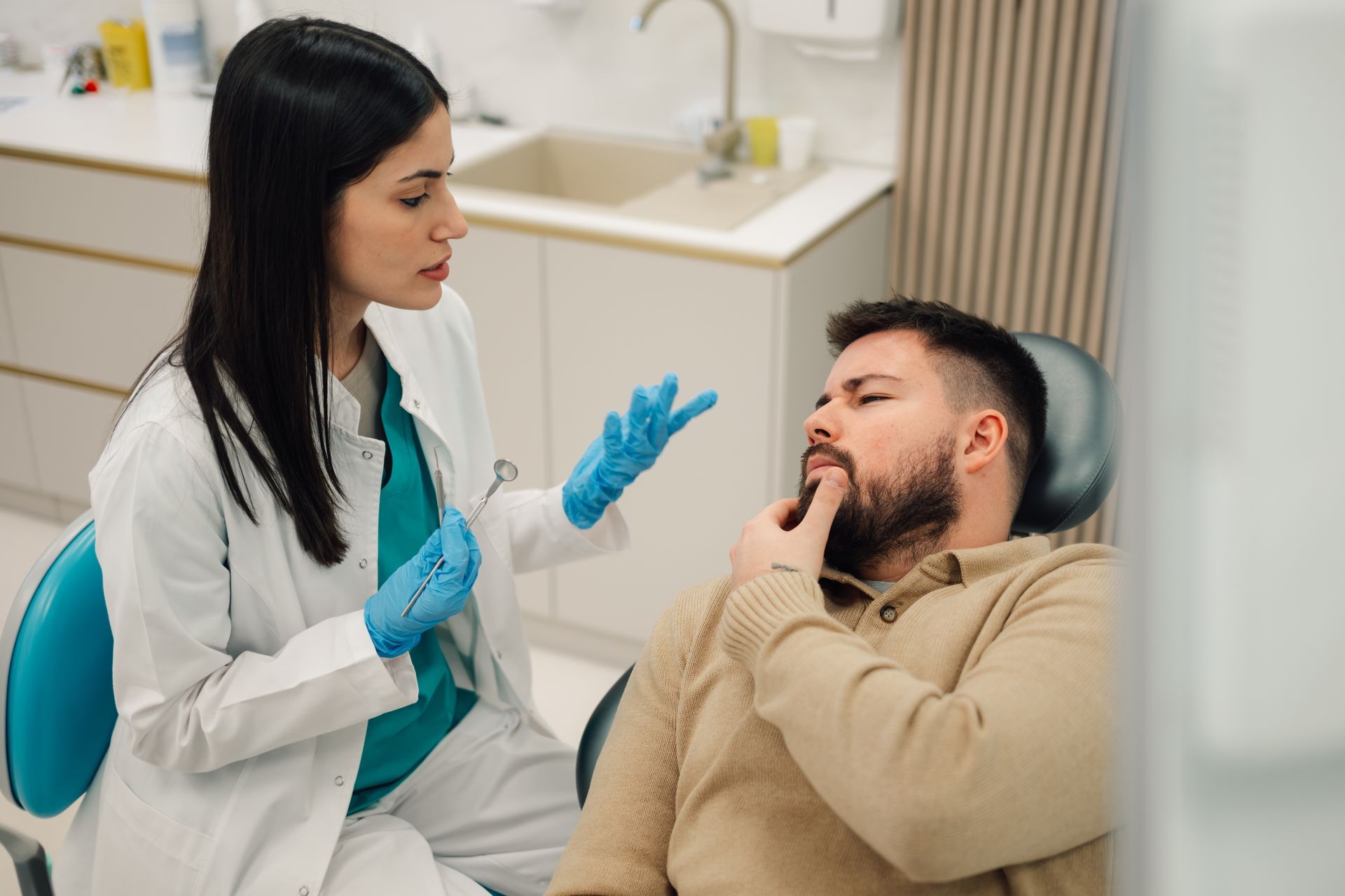 Dentist consulting a patient in a clinic, wearing blue gloves and pointing to his cheek