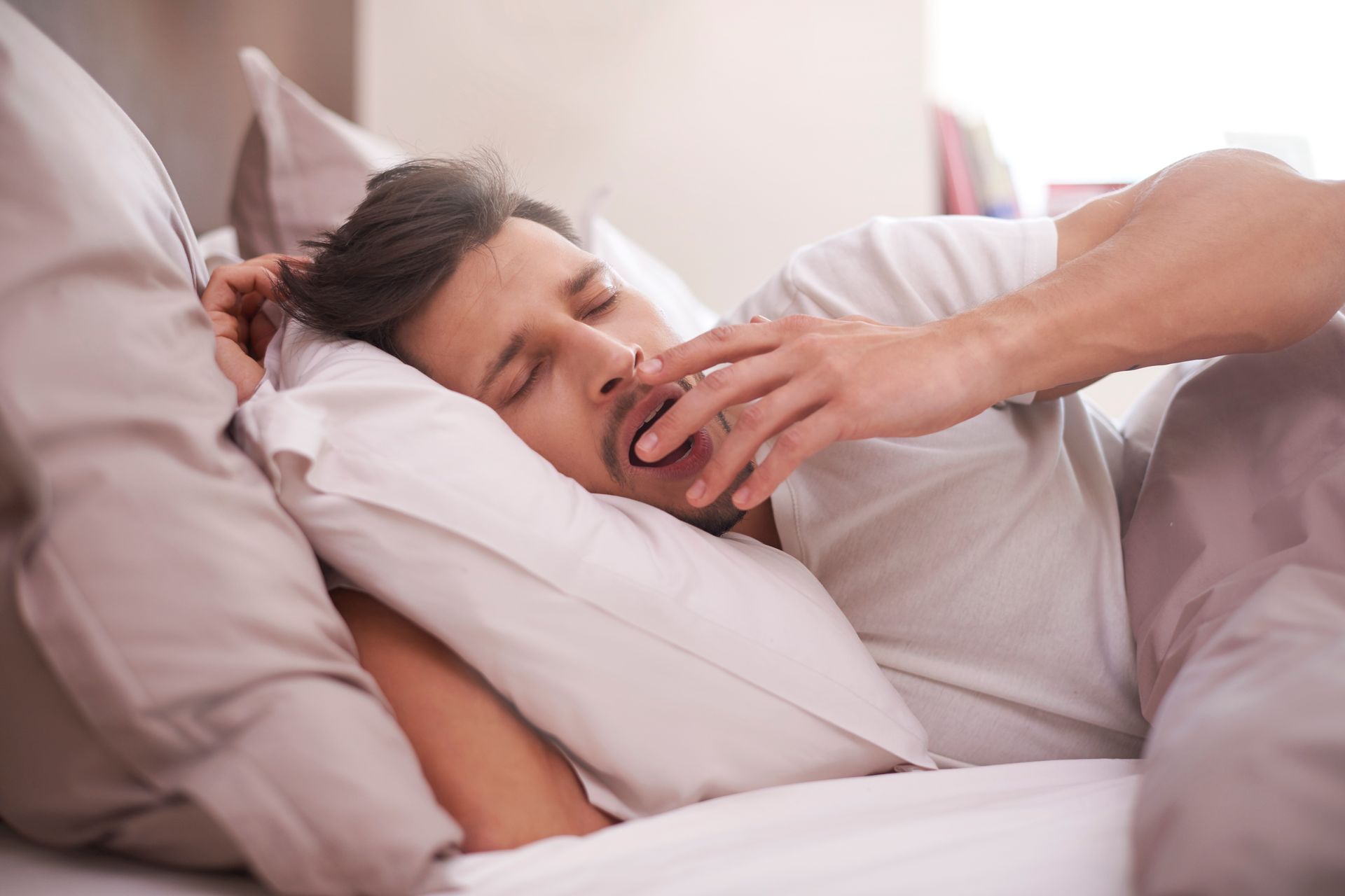 Person resting in bed, asleep with hand near face and white bedding around them.