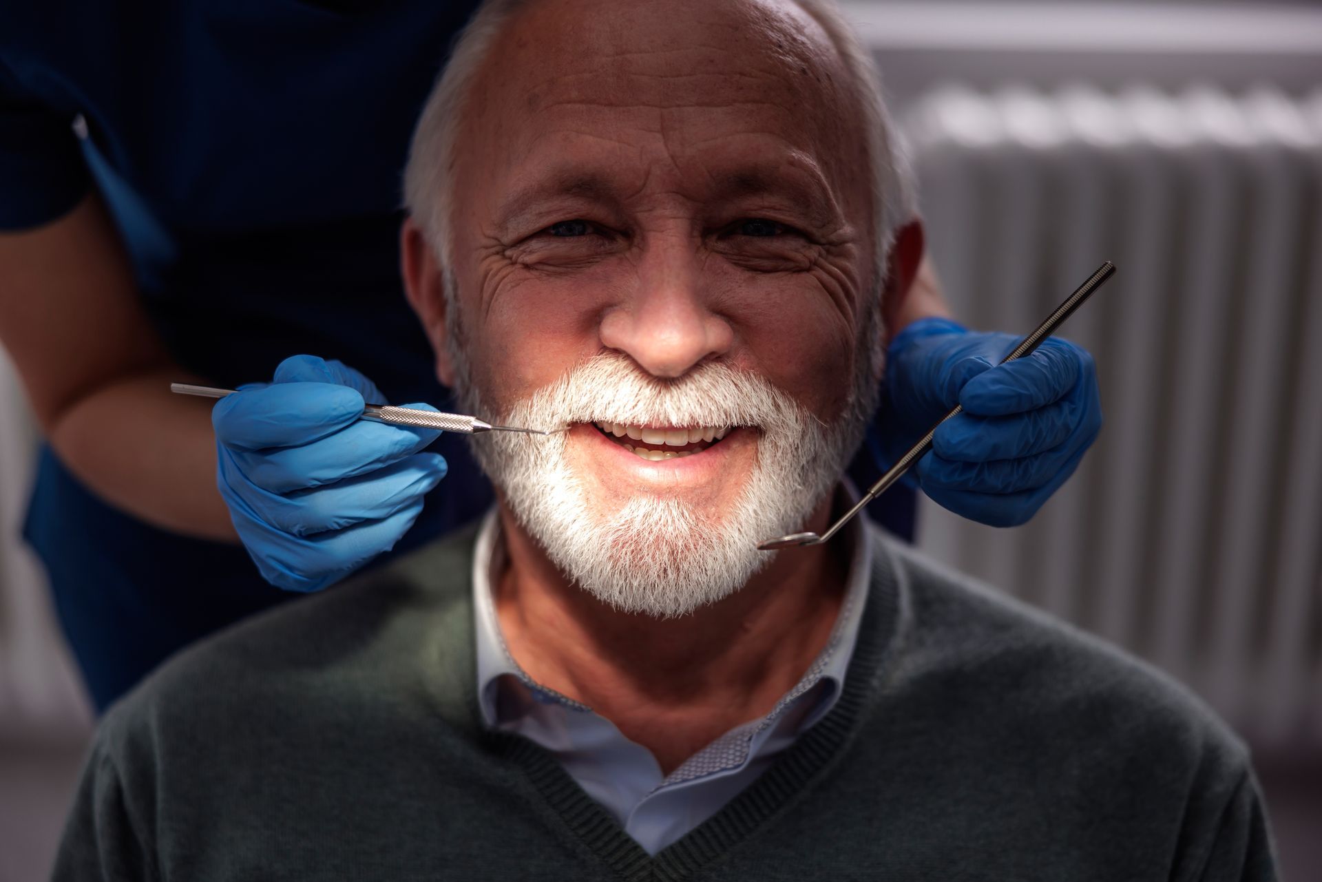 Man at dentist, smiling while tools check teeth. Dentist's hands in blue gloves.