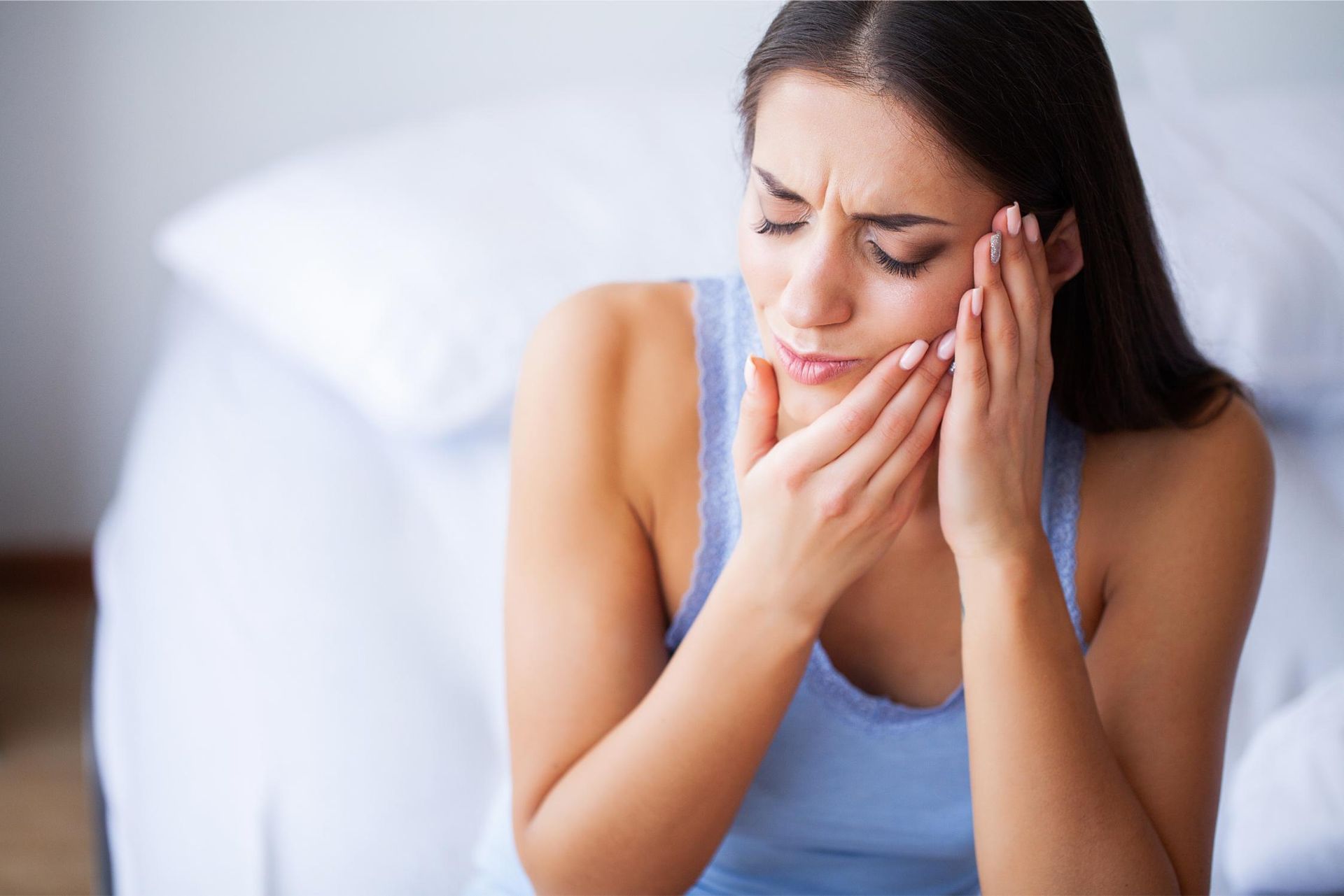 A woman is sitting on a bed with a toothache.