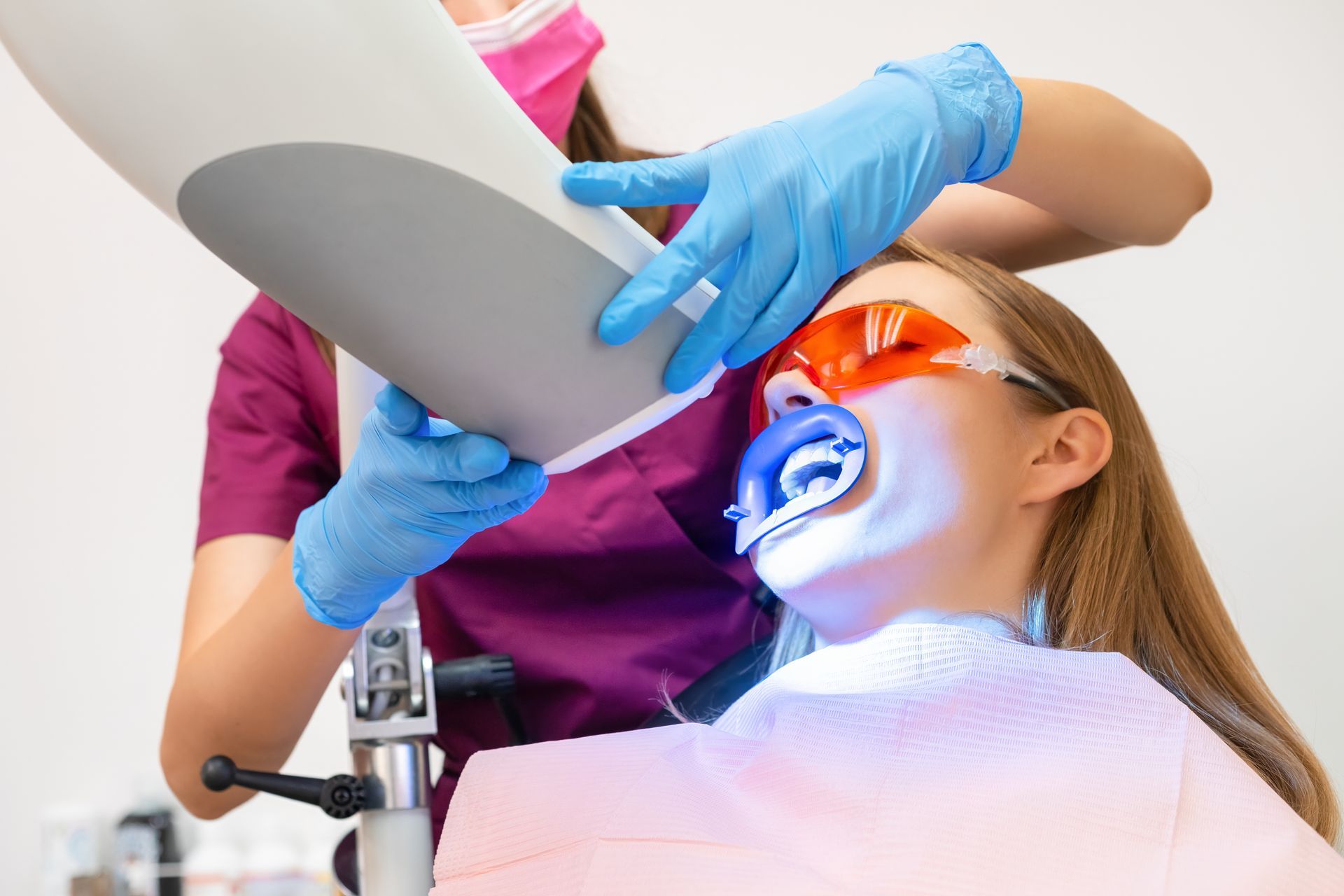 Dentist using blue gloves and a dental light while a patient wears orange protective glasses in a clinic