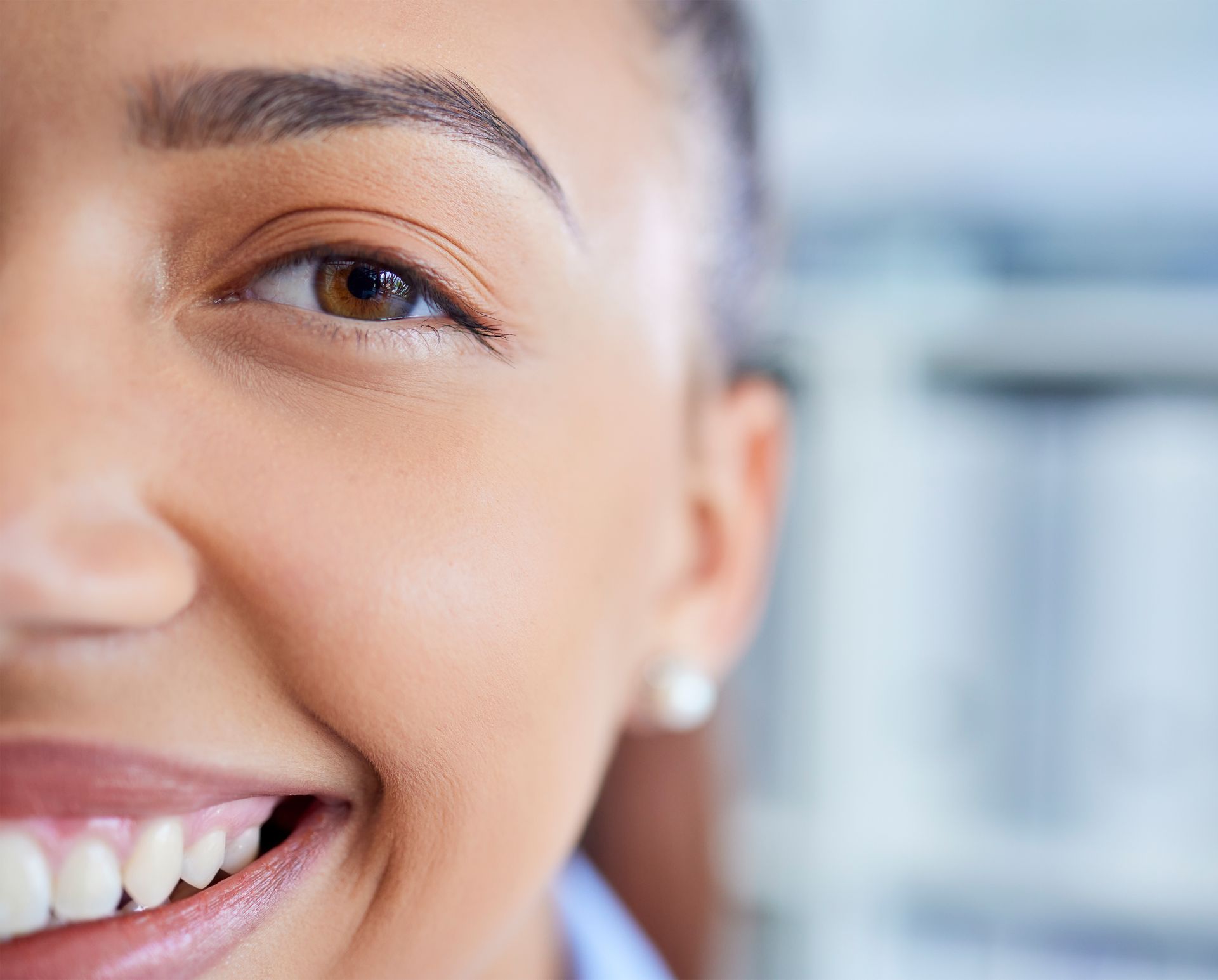 Close-up of a smiling face with a soft-focus background, showing one eye and part of the mouth.