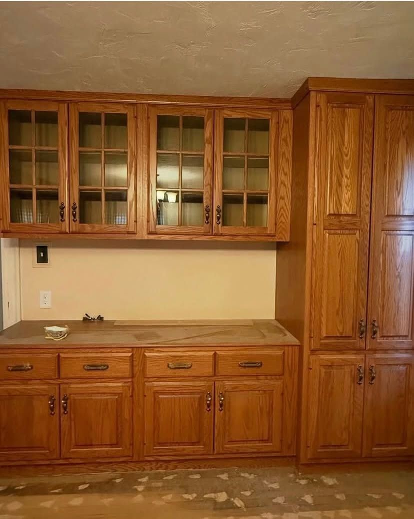 Wooden kitchen cabinets and drawers with glass-front upper cabinets and a beige countertop.