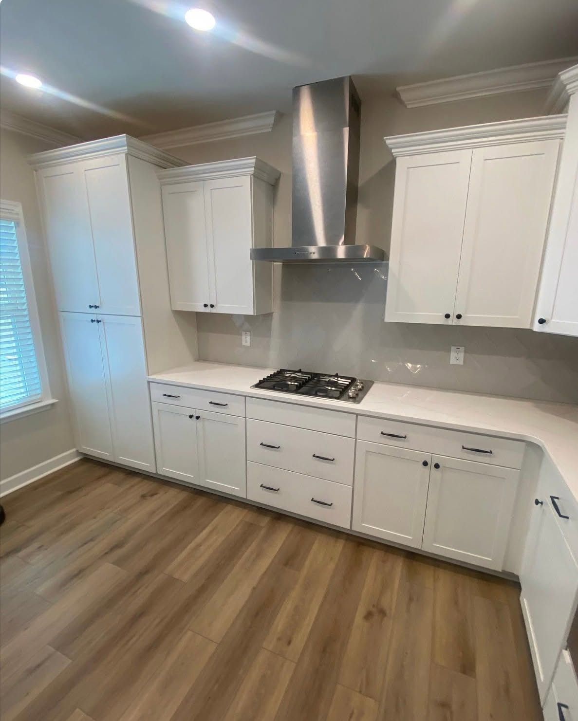 Bright white kitchen with stainless range hood, gas stove, and wood flooring