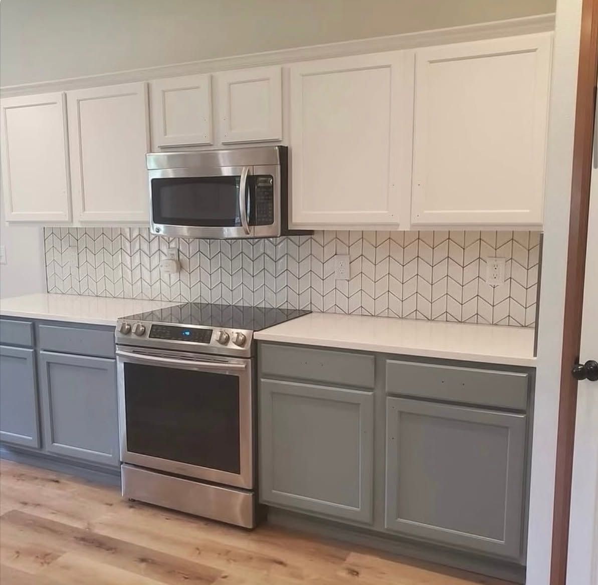 Modern kitchen with white upper cabinets, gray lower cabinets, stainless stove and microwave, and patterned backsplash