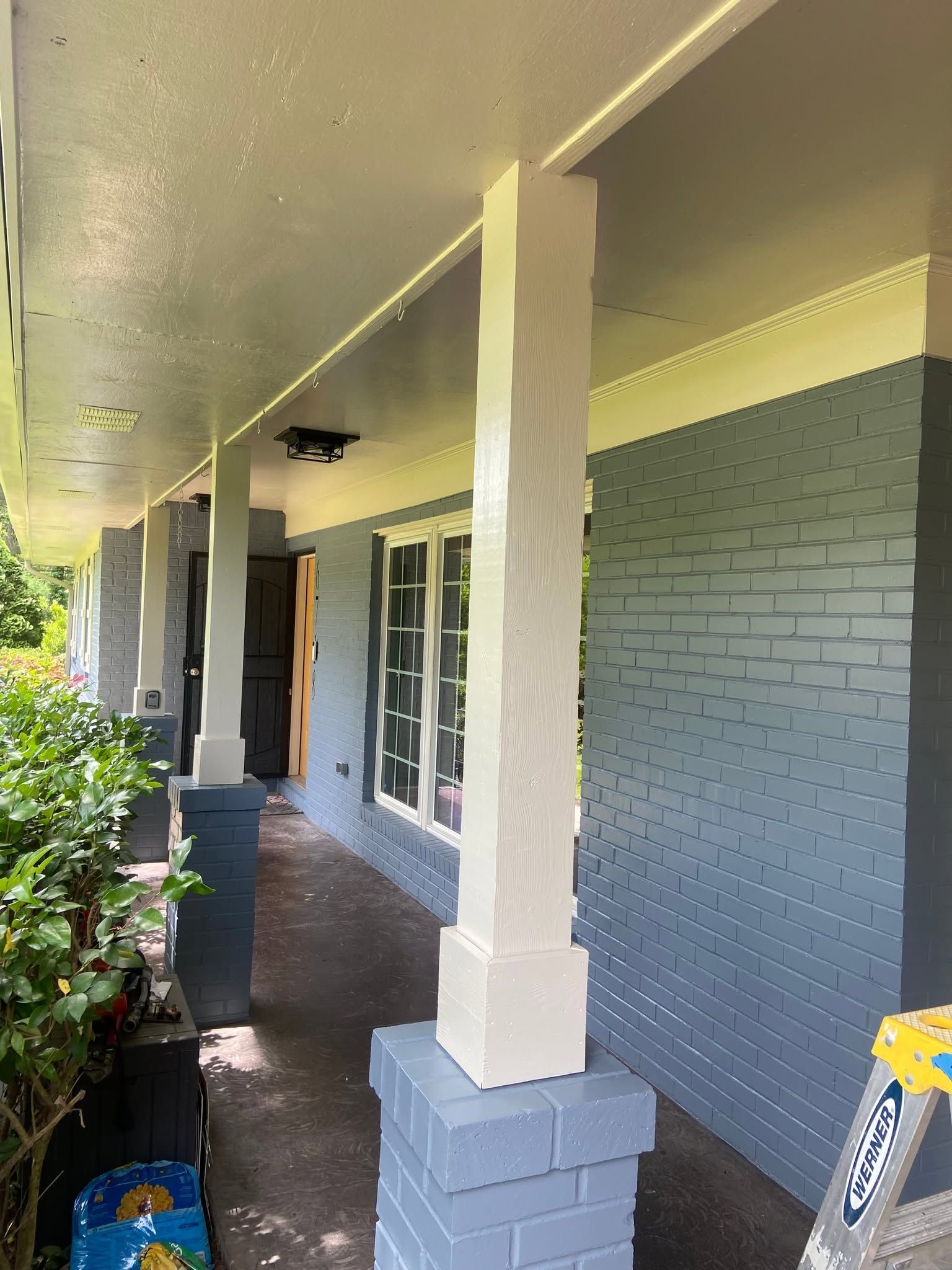 Covered front porch with white columns, gray brick walls, and a dark walkway beside green shrubs