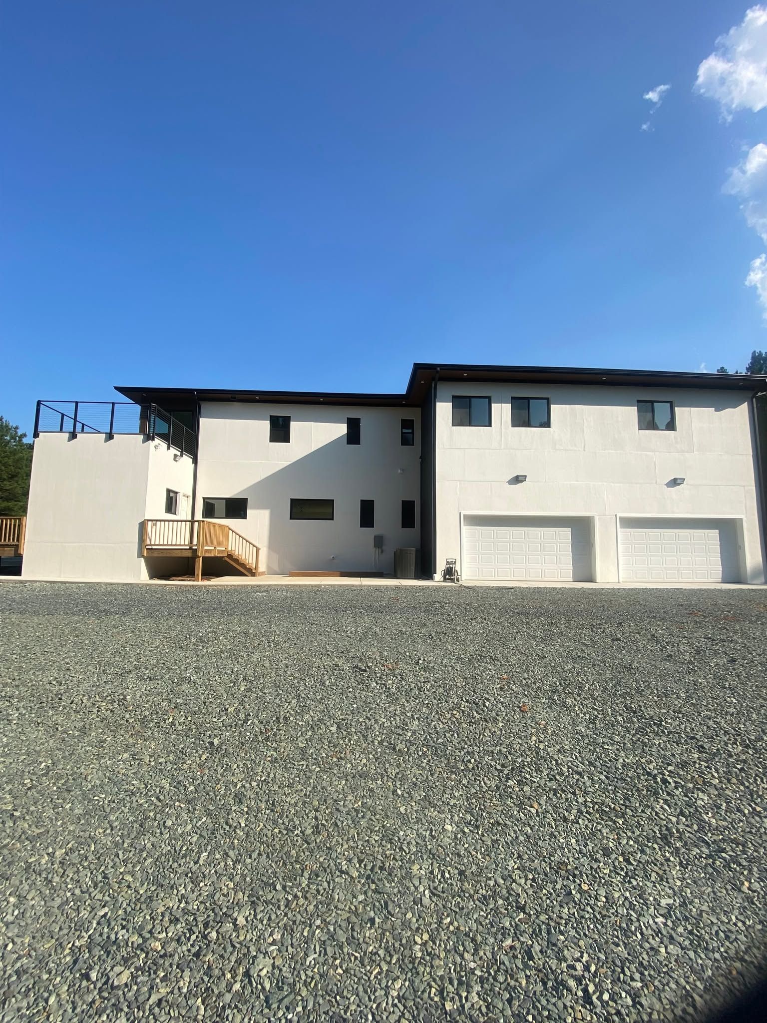 Two-story white house with garage under a clear blue sky, viewed from a gravel lot.