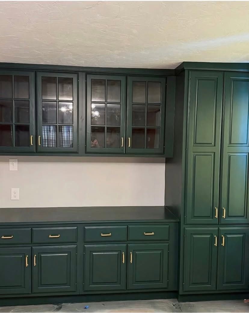 Green kitchen cabinets with glass-front uppers and a built-in desk area against a white wall.