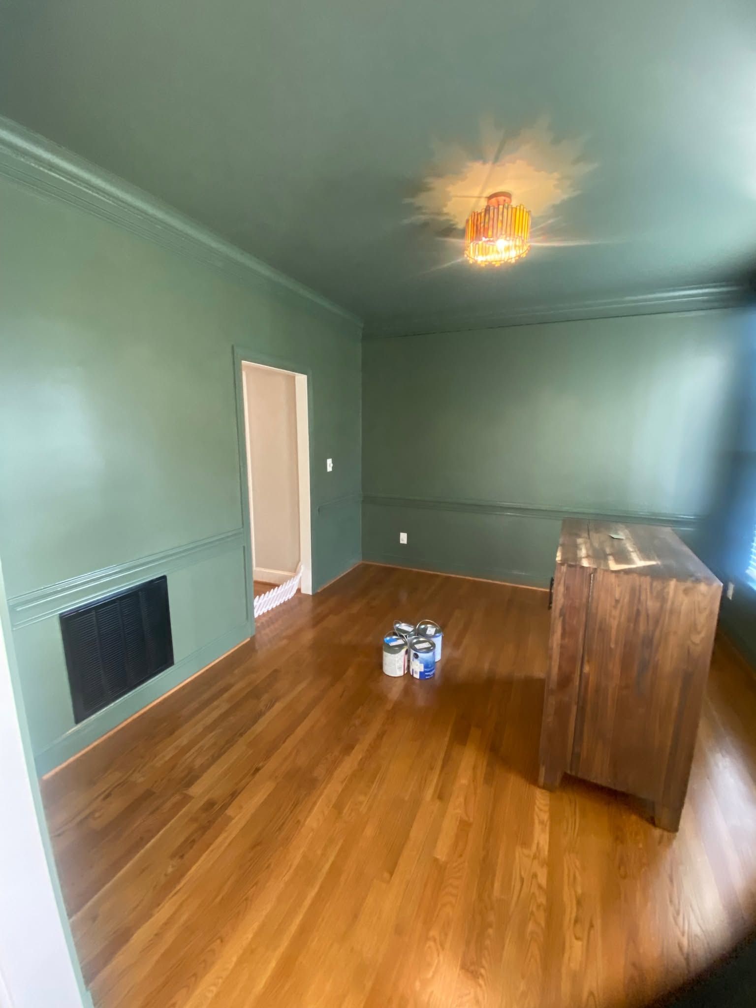 Empty green room with hardwood floor, a doorway, fireplace, and a wooden dresser under a ceiling light.
