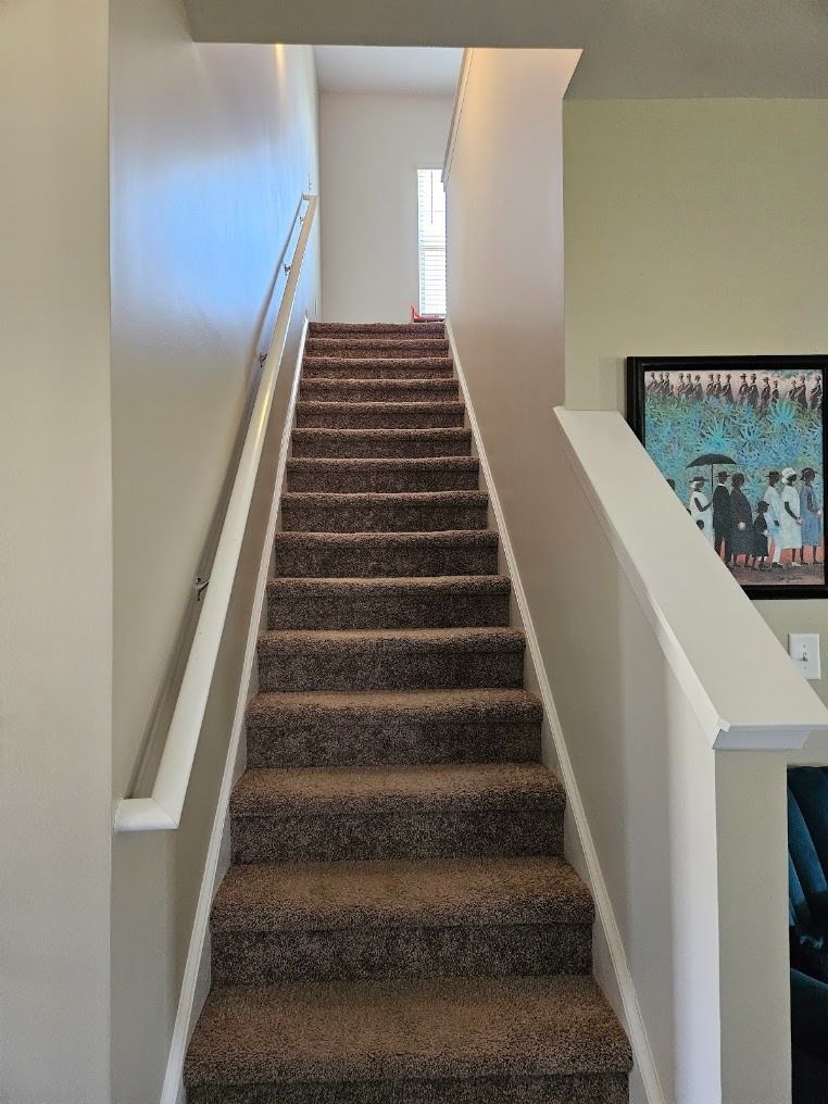 Carpeted staircase with white walls and railings leading to a bright upper landing