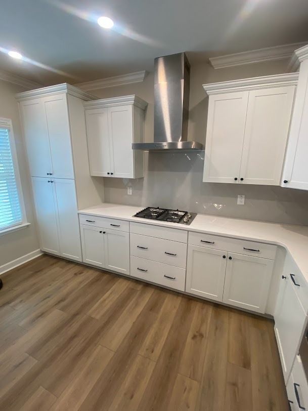 Bright white kitchen with stainless steel range hood, cabinets, and wood flooring